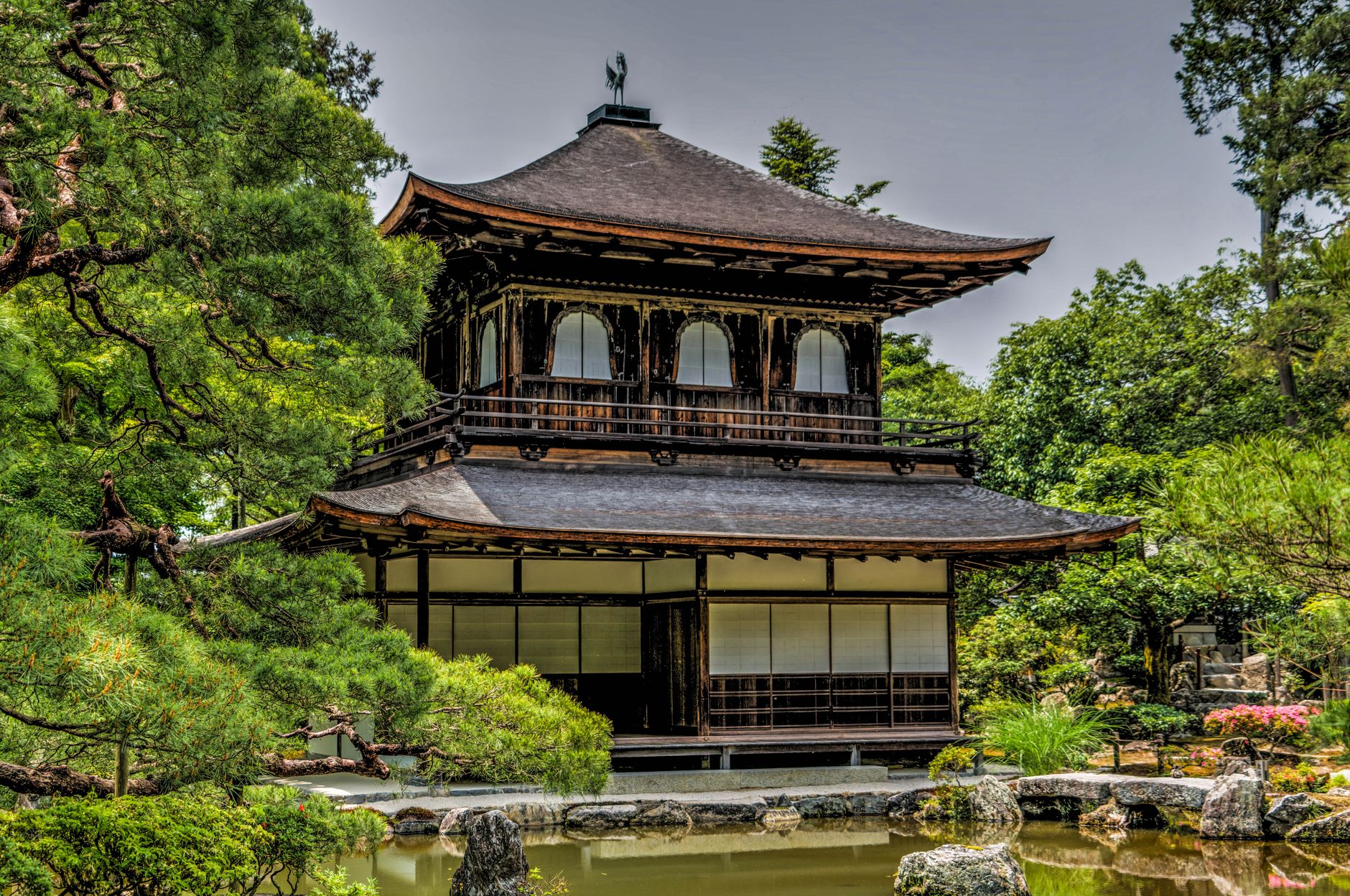 Zen monk in black robes sitting in meditation posture within minimalist temple room with natural light filtering through shoji screens.