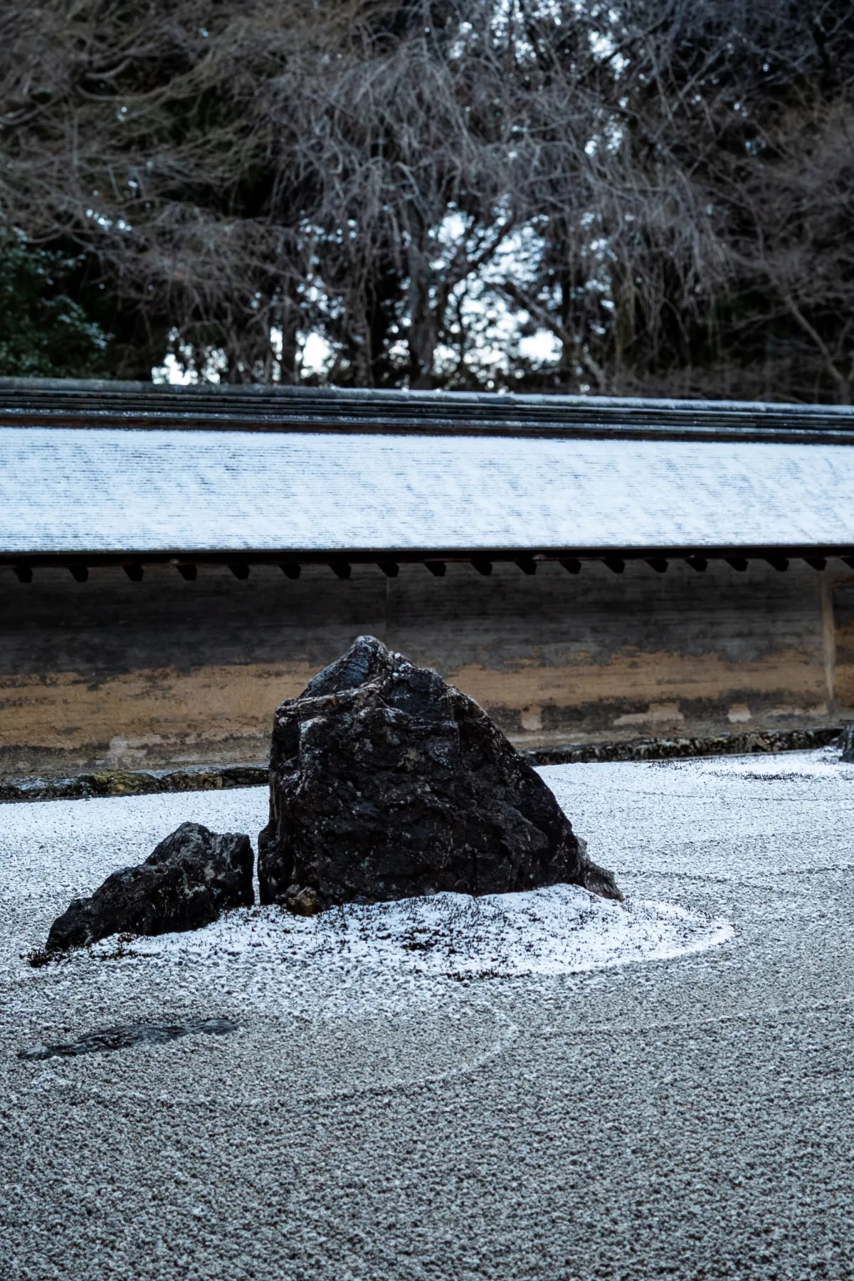 Fifteen weathered stones arranged in carefully raked white gravel at Ryoanji Temple's minimalist Zen rock garden in Kyoto.