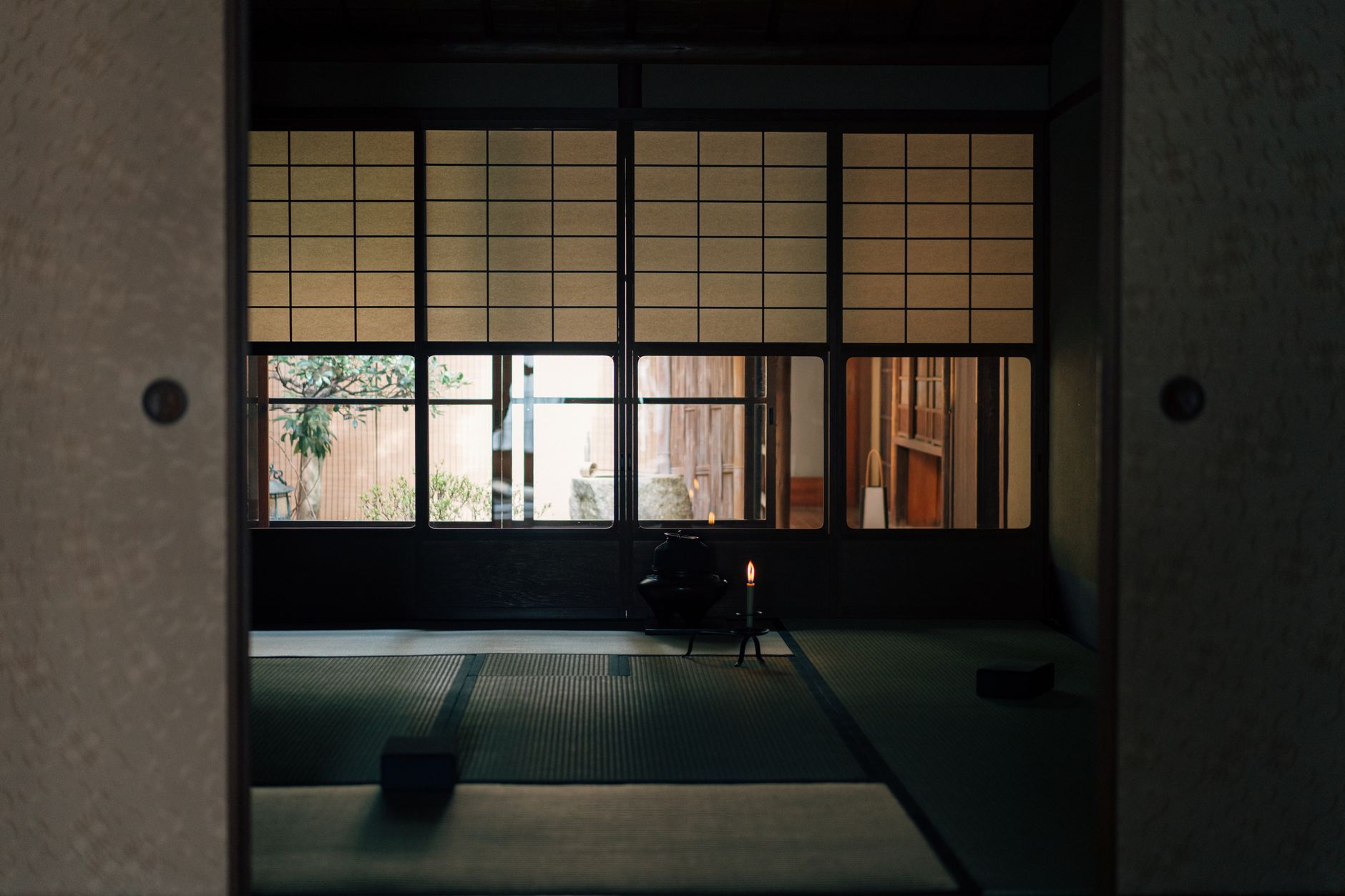 A person in traditional kimono bowing to enter through the low square entrance of a Japanese tea house.
