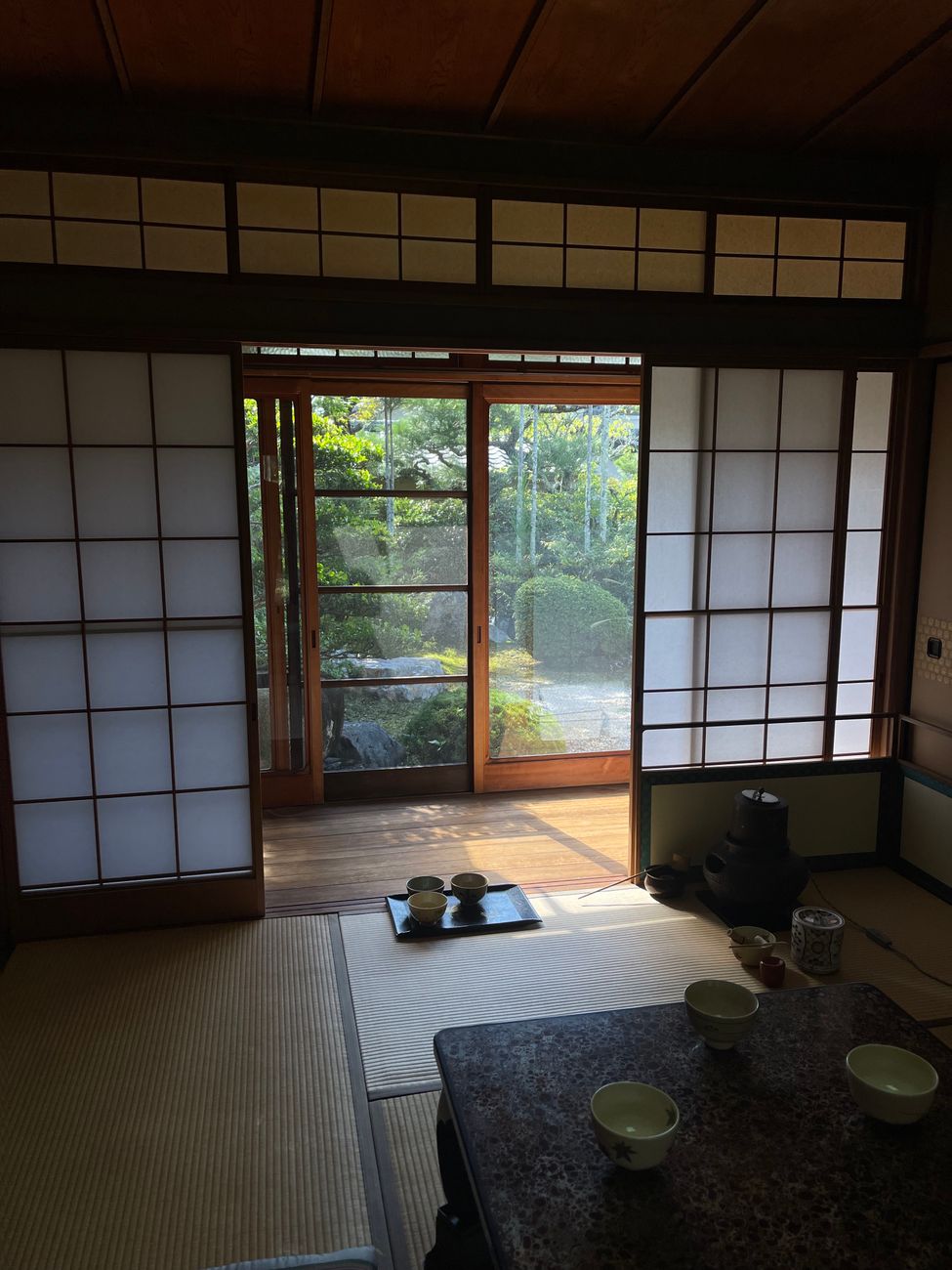 A person in traditional kimono bowing to enter through the low square entrance of a Japanese tea house.