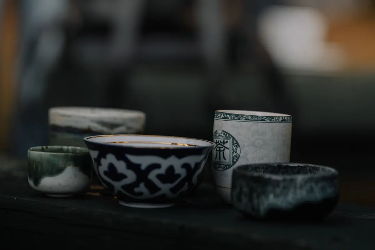 Hands cupping a warm yunomi tea bowl, fingers wrapped around smooth ceramic, steam rising from green tea inside.