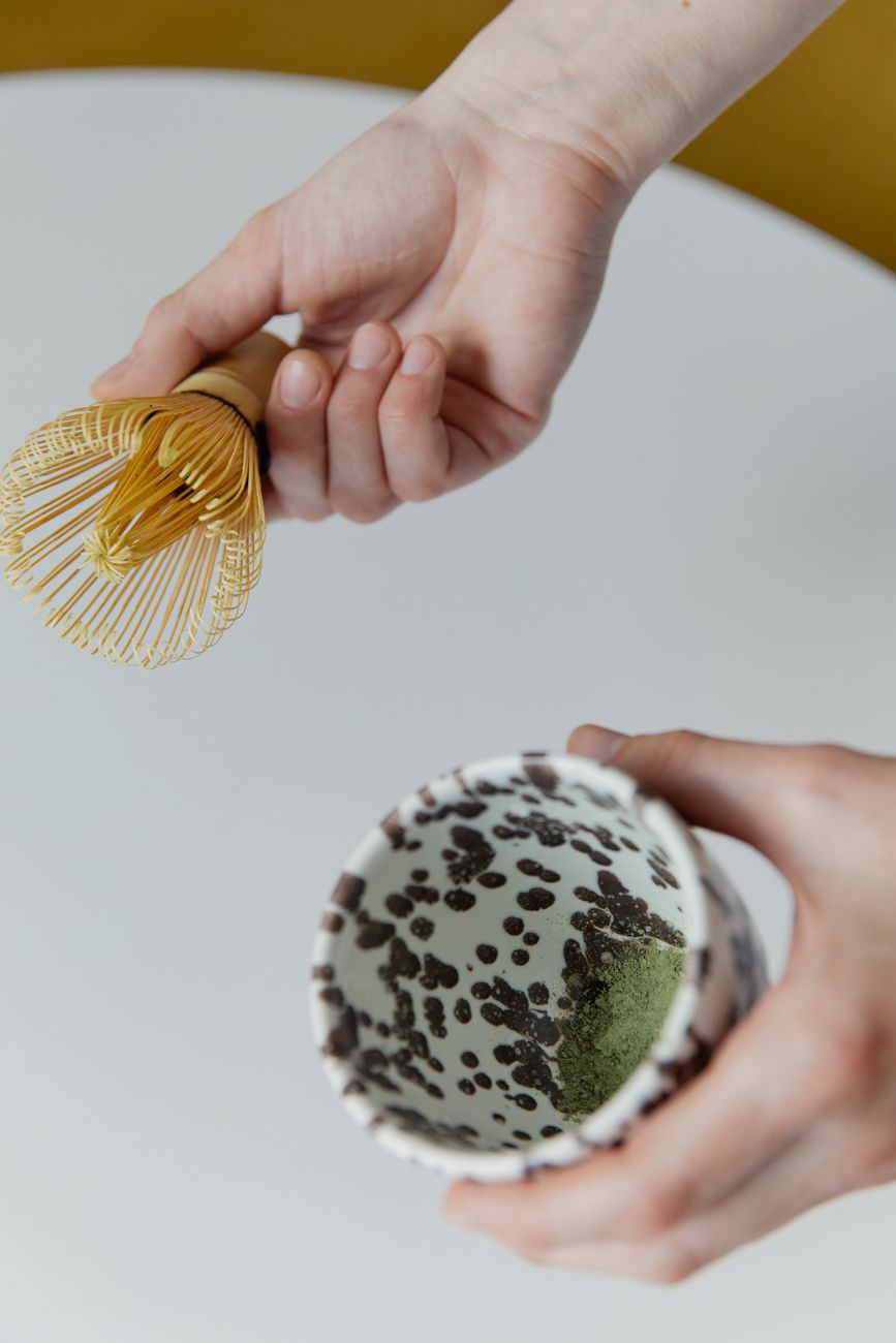 Hands cupping a warm yunomi tea bowl, fingers wrapped around smooth ceramic, steam rising from green tea inside.