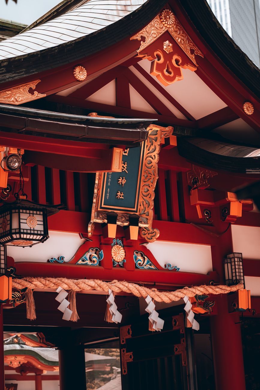 Wooden torii gate frames a gravel path leading to a traditional Shinto shrine surrounded by tall cedar trees.