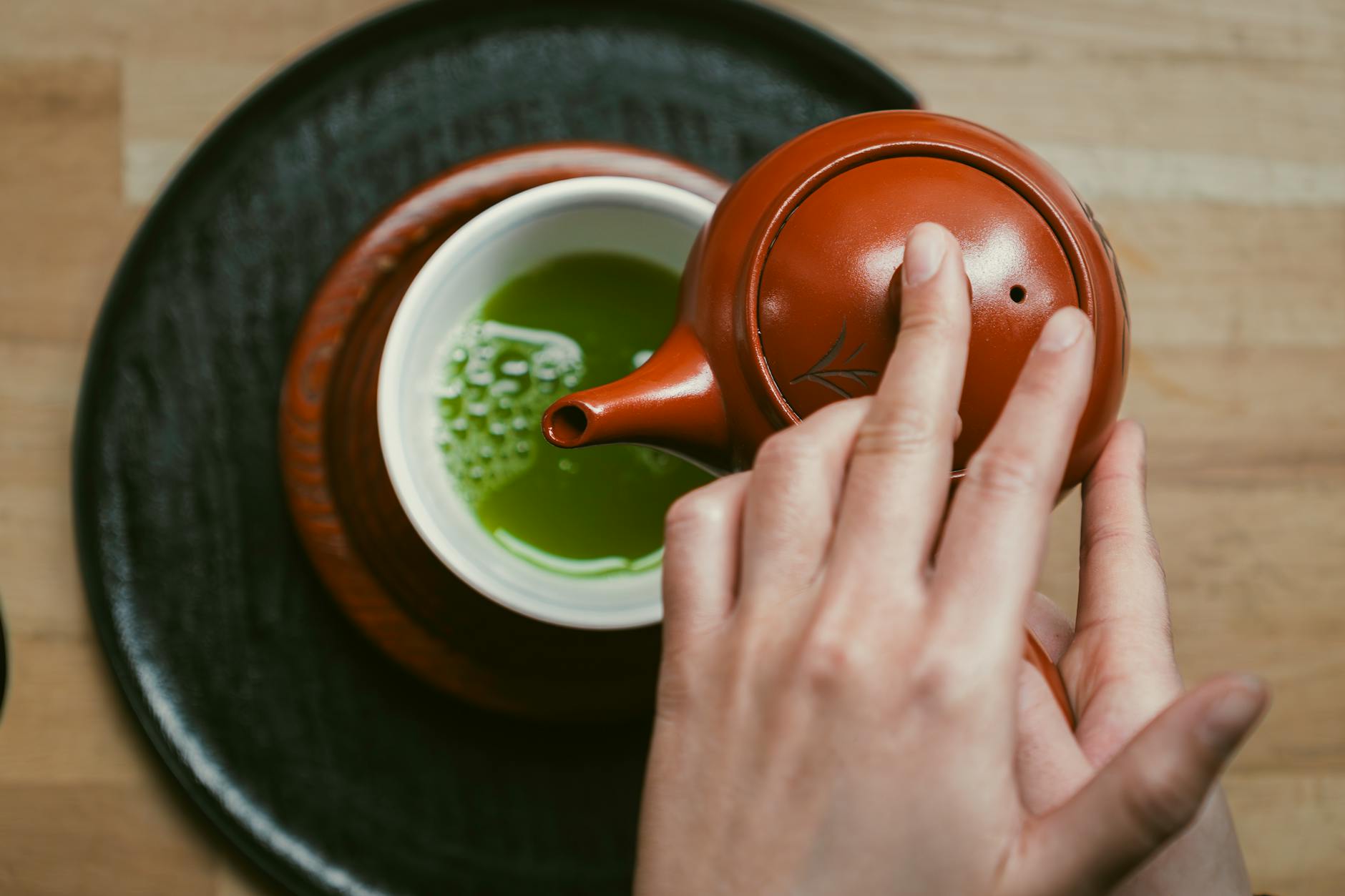 Vibrant green matcha powder in a ceramic bowl beside a bamboo whisk on a minimalist white surface.