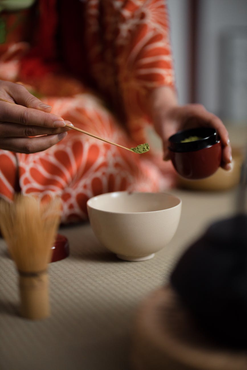 Vibrant green matcha powder in a ceramic bowl beside a bamboo whisk on a minimalist white surface.