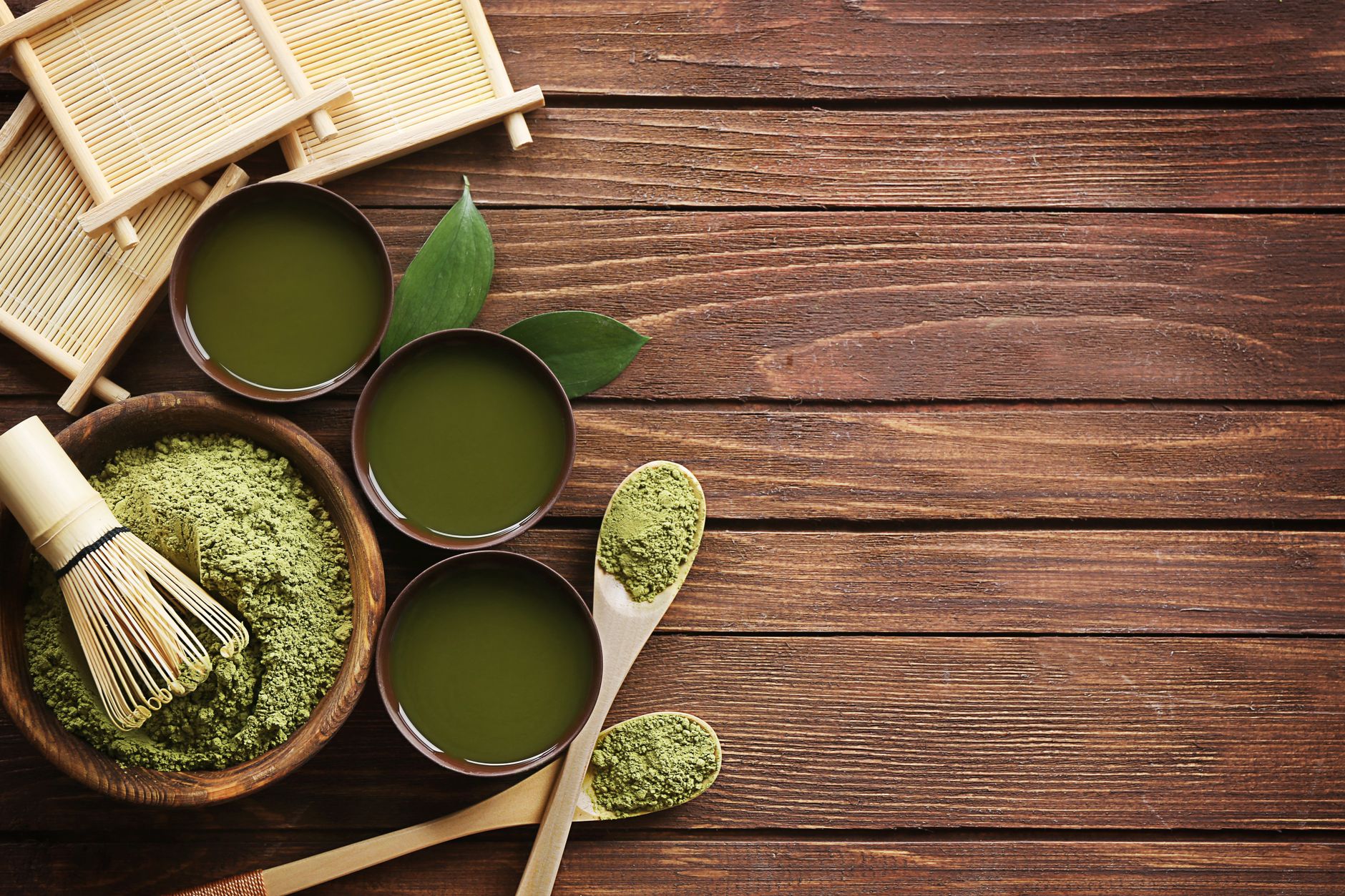 Vibrant green matcha powder in a ceramic bowl beside a bamboo whisk on a wooden table with natural light.