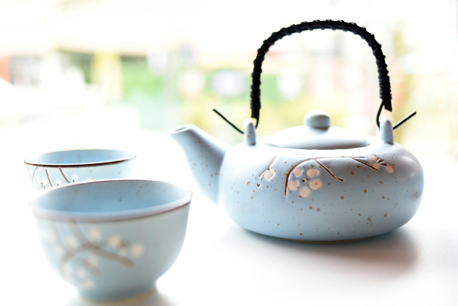 Traditional Japanese kyusu teapot with side handle pouring green tea into a small ceramic cup on wooden table.
