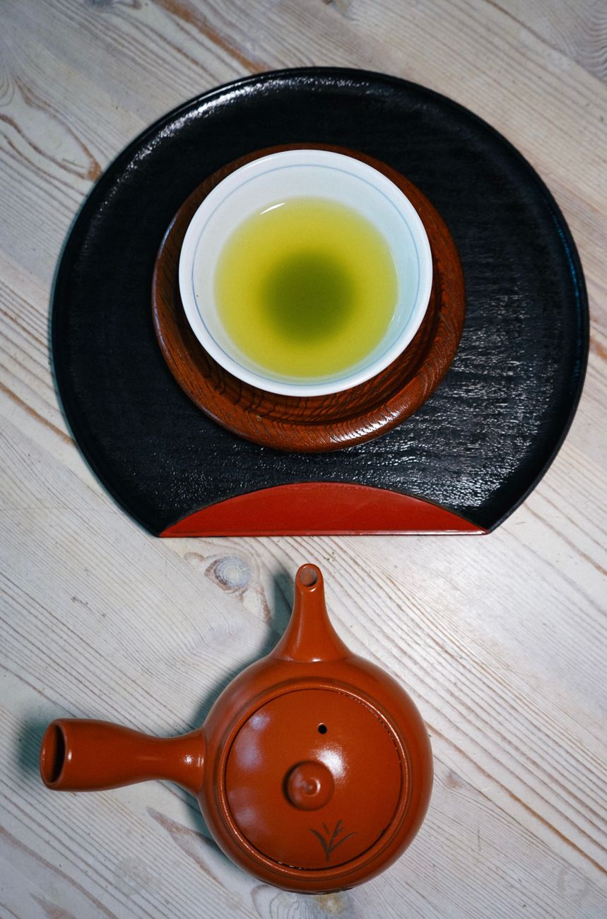 Traditional Japanese kyusu teapot with side handle pouring green tea into a small ceramic cup on wooden table.
