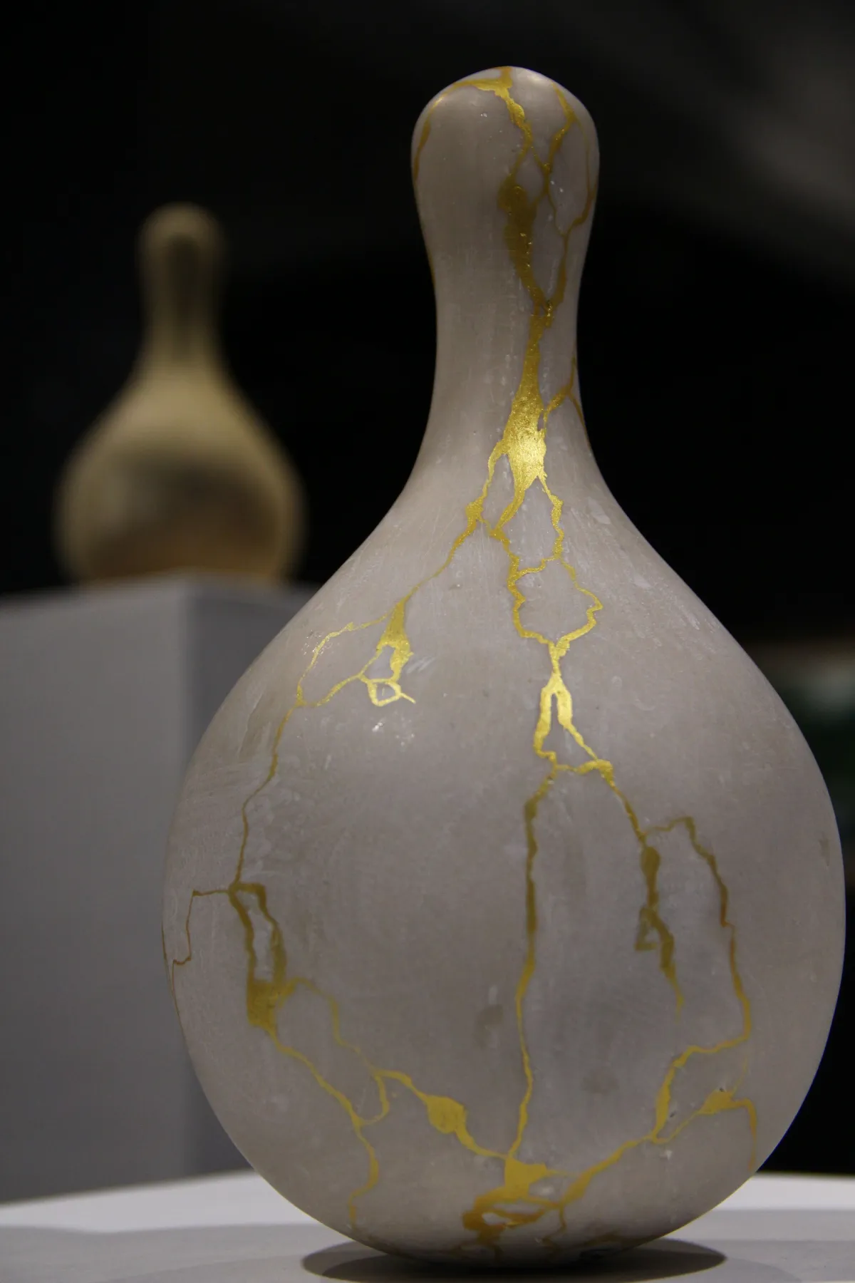 Hands applying gold lacquer to a cracked ceramic bowl on a wooden workspace with kintsugi tools and materials nearby.