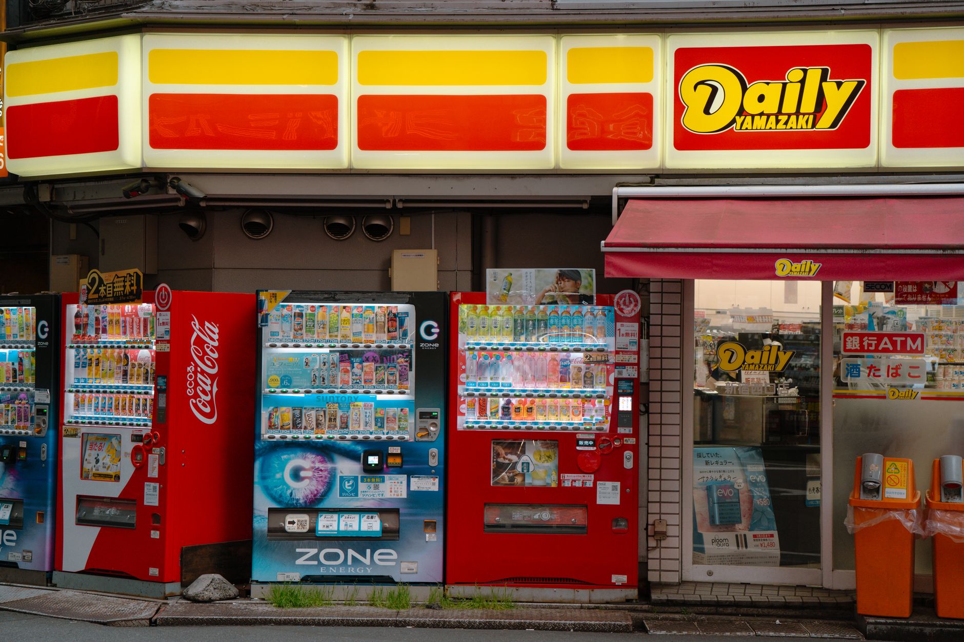 Row of illuminated vending machines on a quiet Tokyo street at night, displaying colorful drinks and snacks through glass fronts.