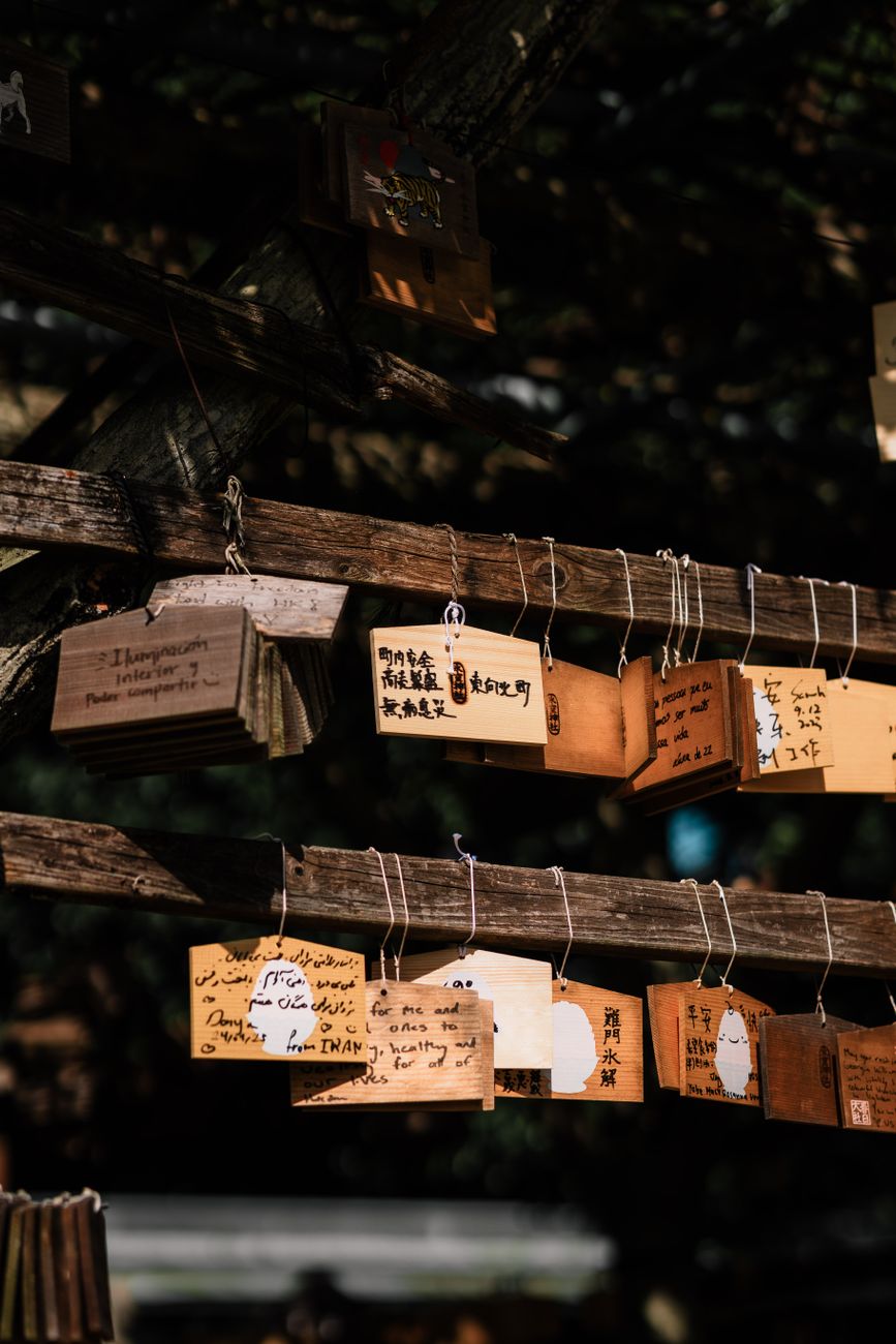 Folded white paper fortunes tied to wooden frame at Japanese shrine with red torii gate visible in background.
