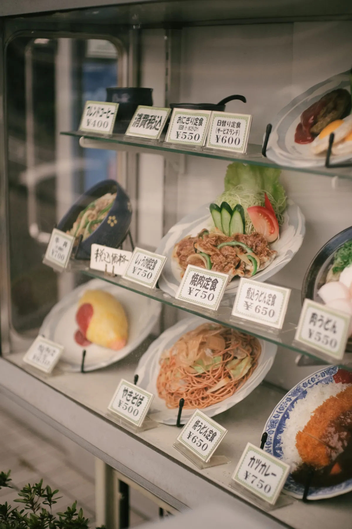 Colorful plastic food samples including ramen, sushi, and tempura arranged in a Japanese restaurant display window in Tokyo.