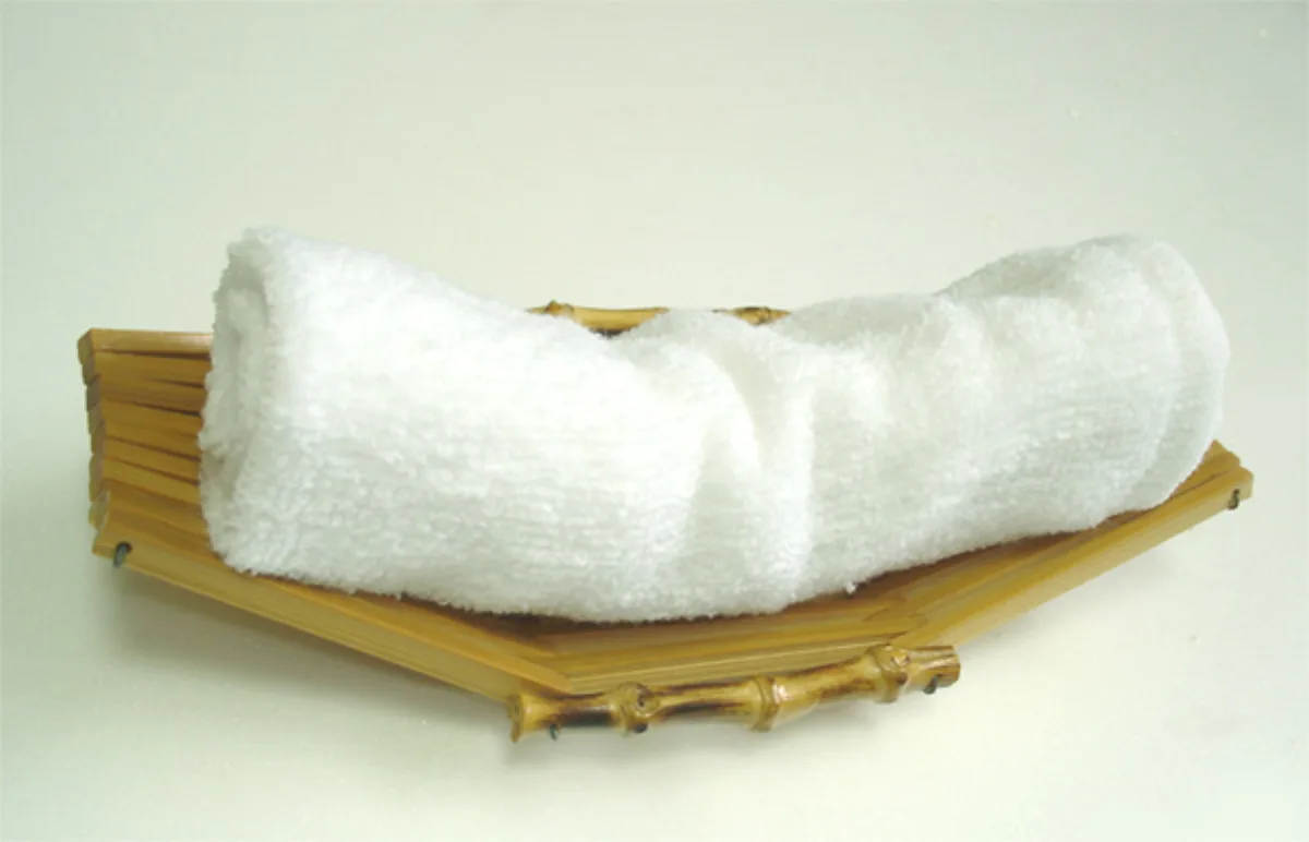White cotton oshibori hand towel rolled on a ceramic tray beside chopsticks at a traditional Japanese restaurant table setting.