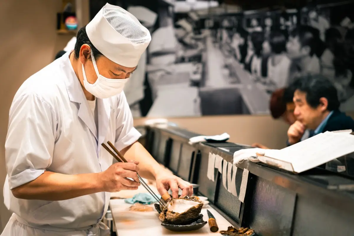 A Japanese restaurant staff member politely handing a bill on a small tray to a seated customer