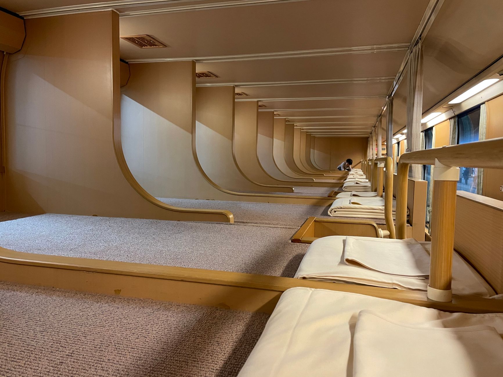 A row of stacked sleeping pods with curtains in a minimalist Japanese capsule hotel interior with soft lighting.