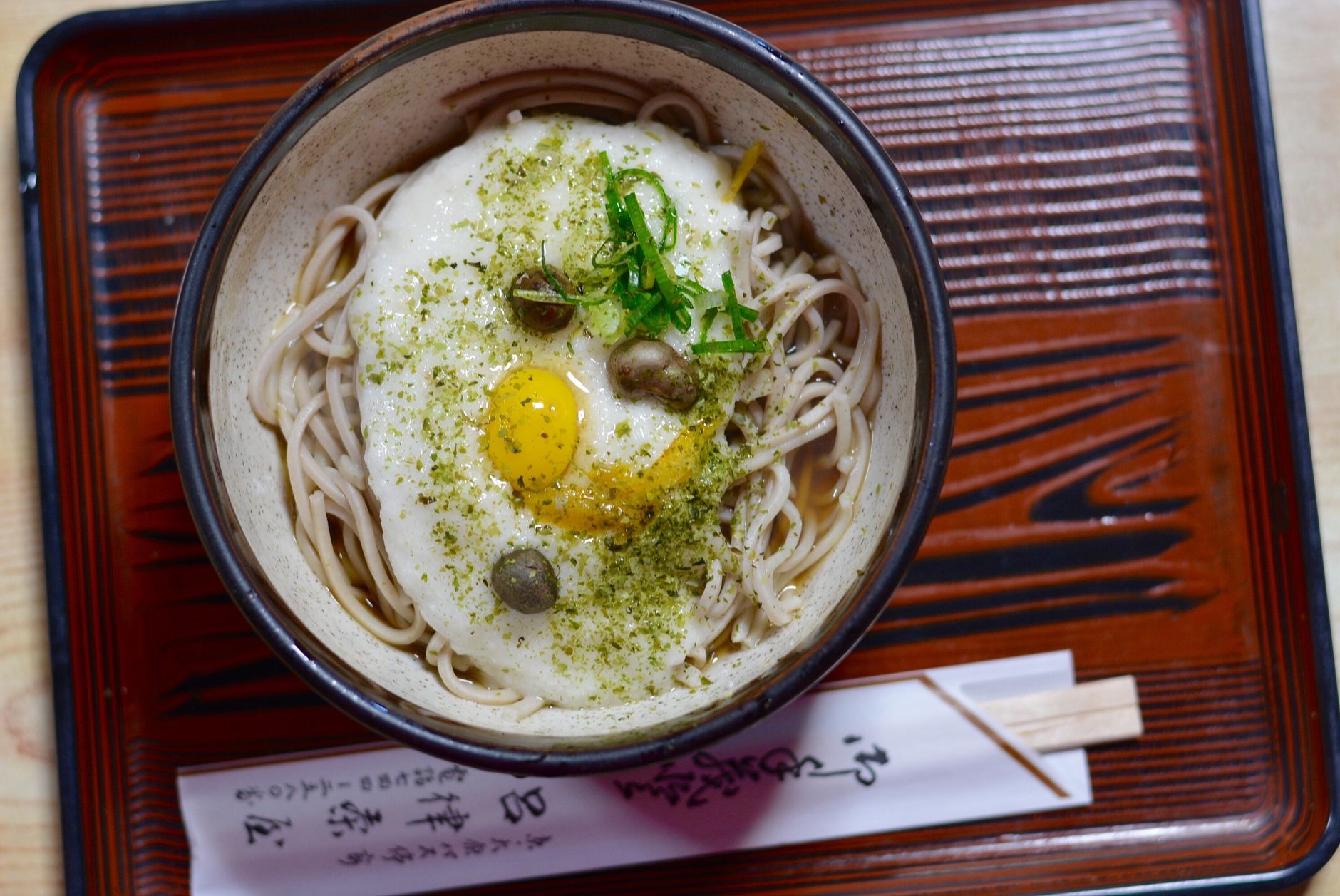 Person using chopsticks to lift steaming ramen noodles from a ceramic bowl, creating visible steam in a traditional Japanese setting.