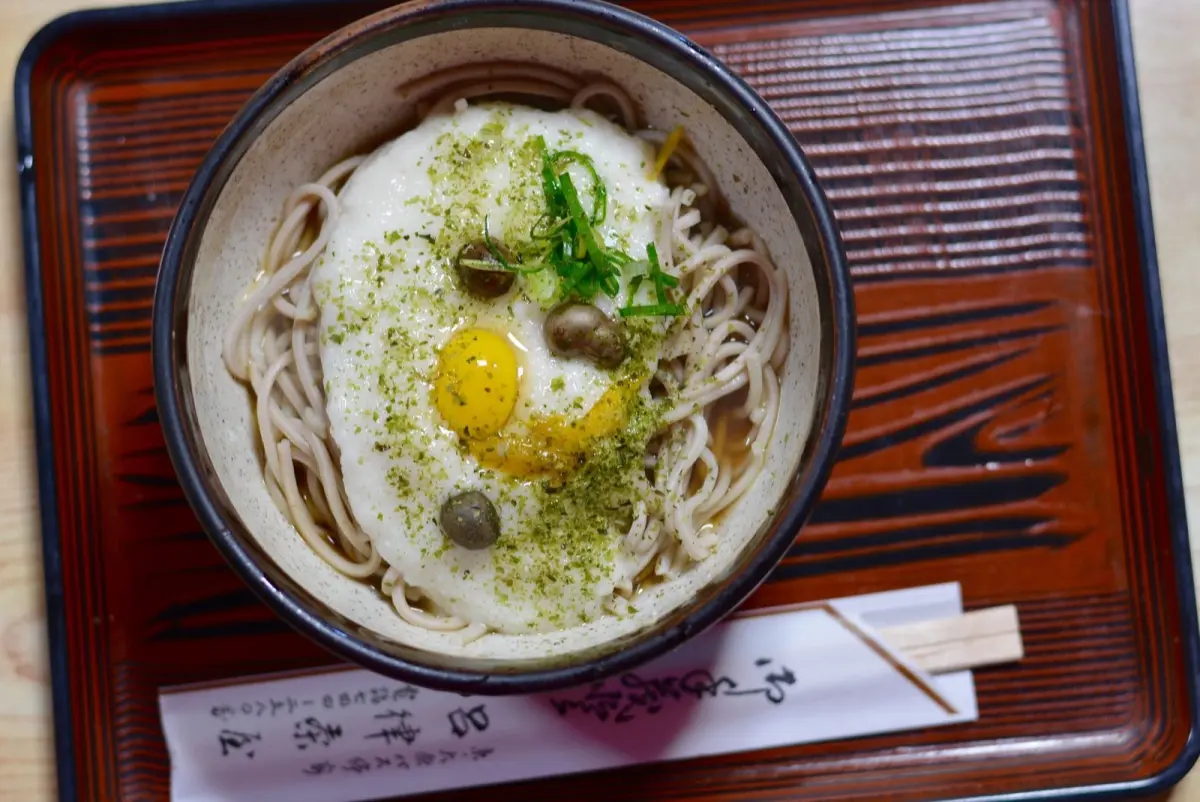 A person lifting ramen noodles from a steaming bowl with chopsticks in a Japanese noodle shop