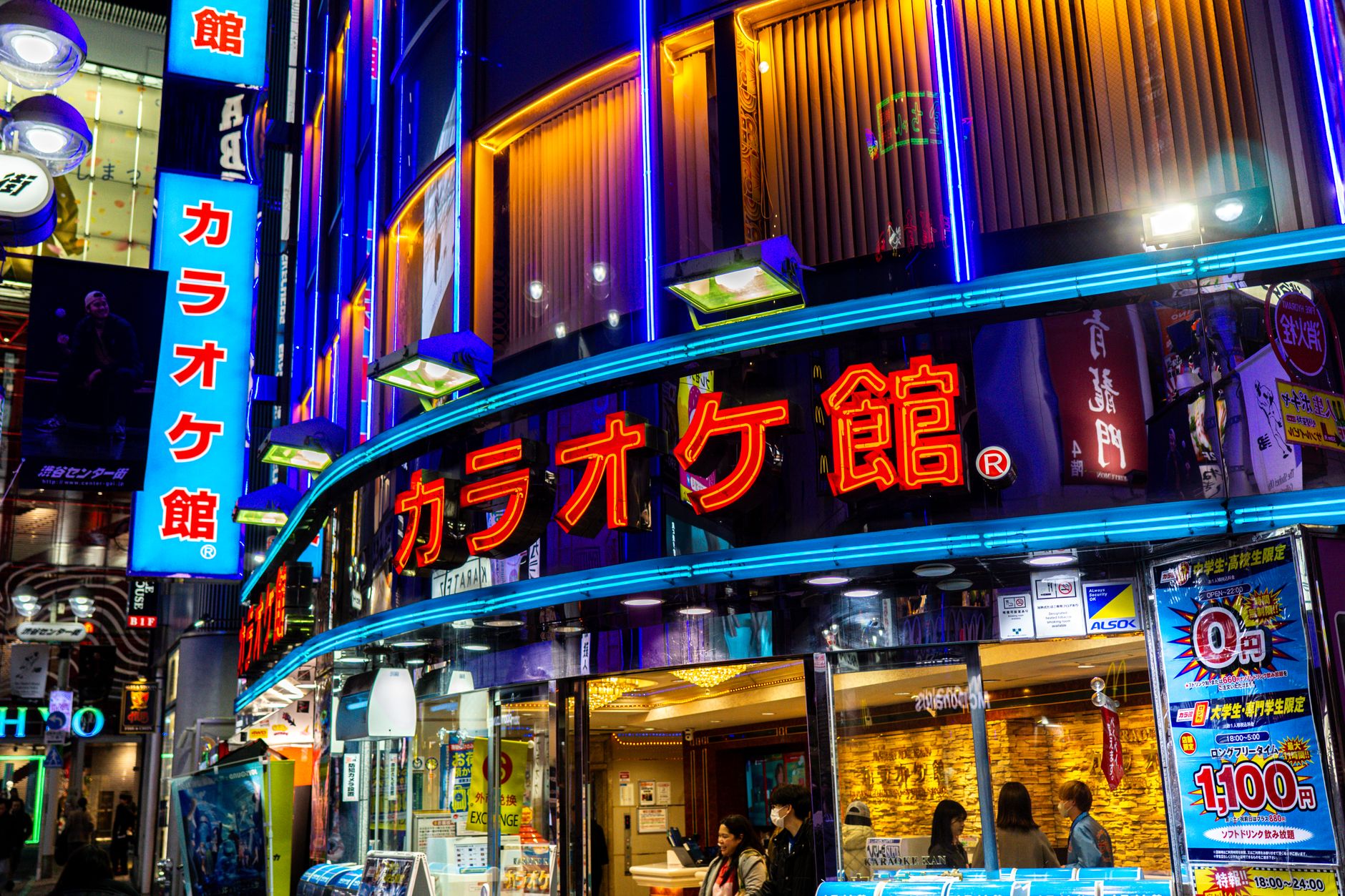 Quiet Tokyo street illuminated by warm vending machine lights and neon signs with no pedestrians visible at midnight.