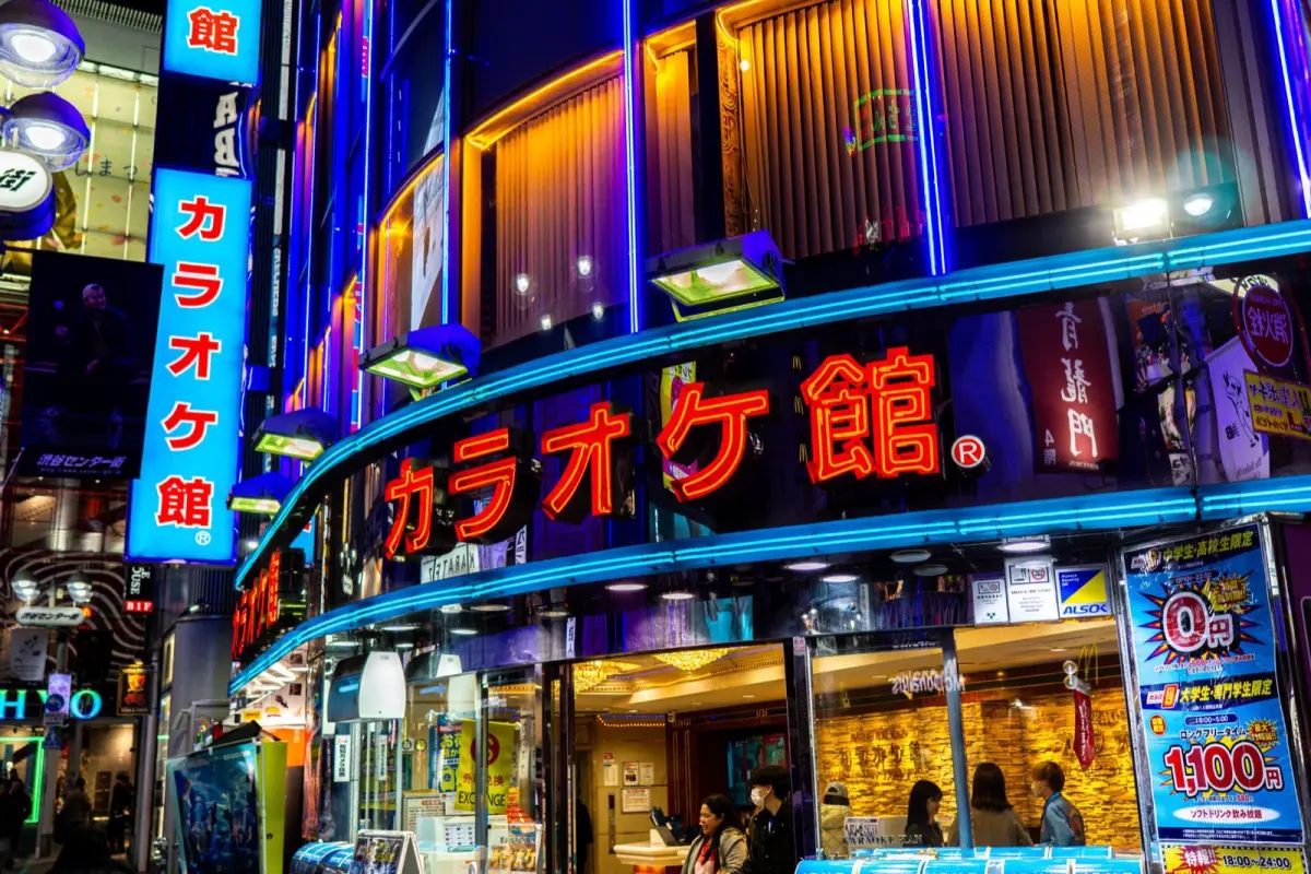 Quiet Tokyo street illuminated by warm vending machine lights and neon signs with no pedestrians visible at midnight.
