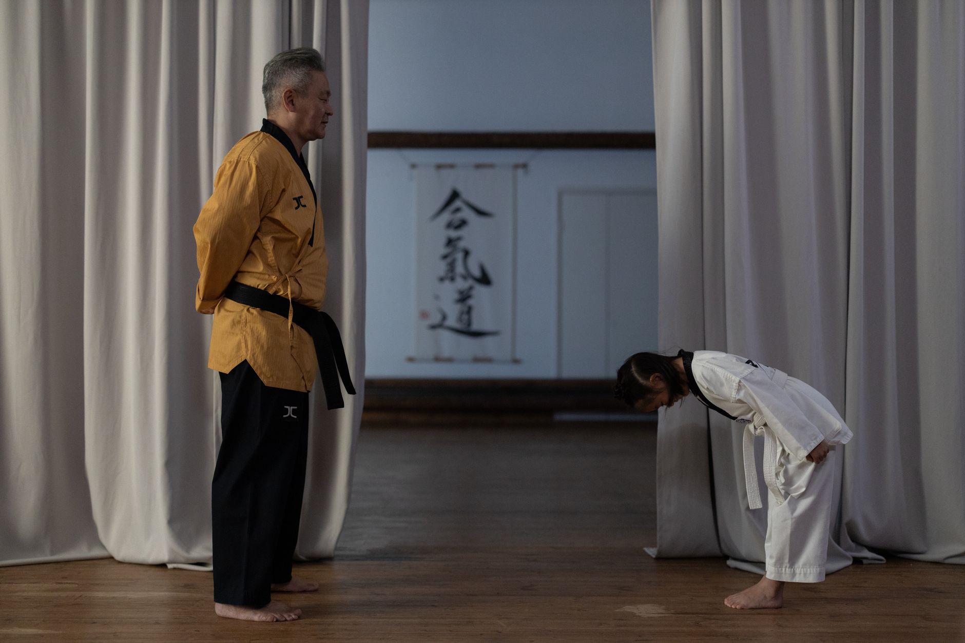 Two Japanese businesspeople bowing to each other at different angles on a city street in formal attire.