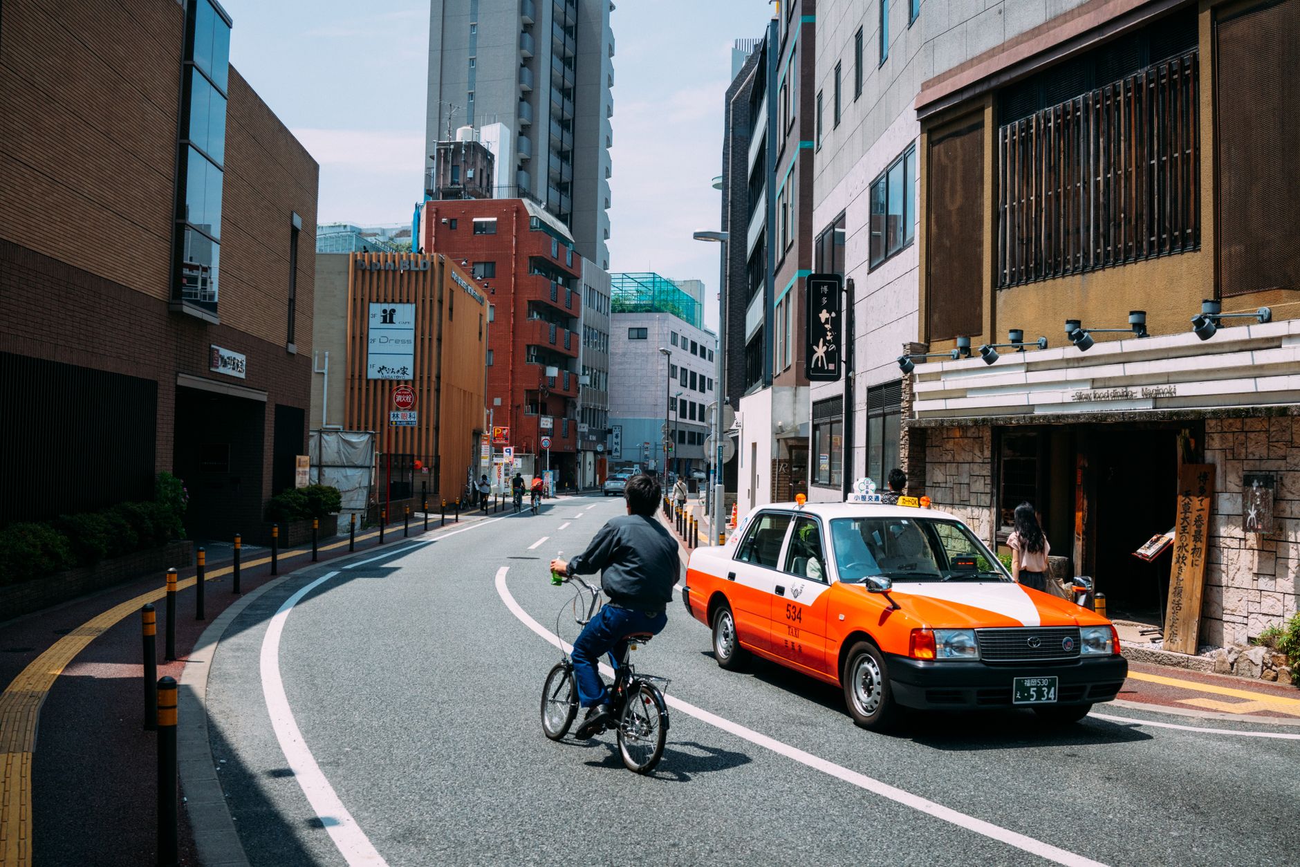 Japanese taxi driver operating automatic door mechanism from inside vehicle on Tokyo city street during daytime.