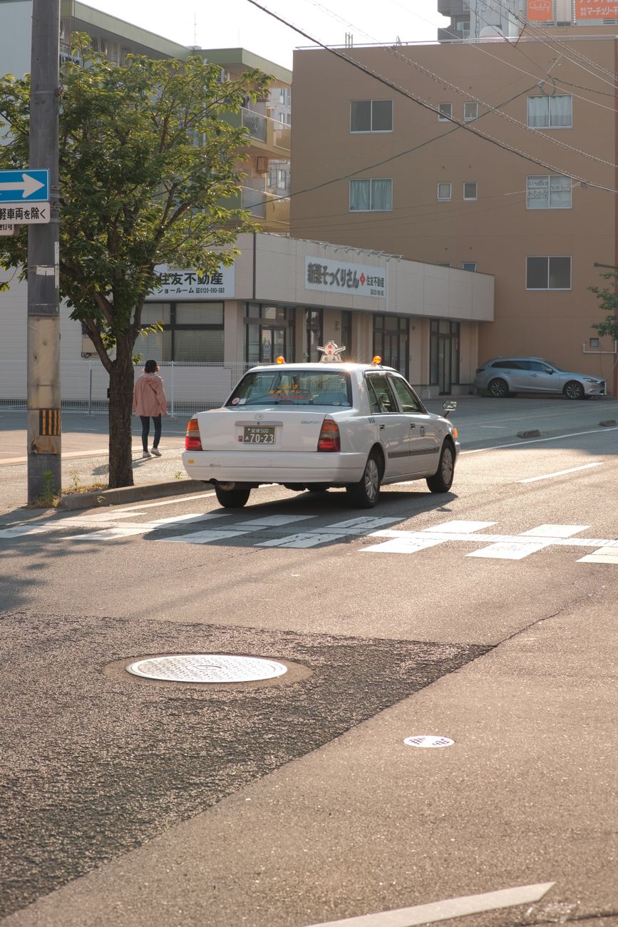 Japanese taxi driver operating automatic door mechanism from inside vehicle on Tokyo city street during daytime.