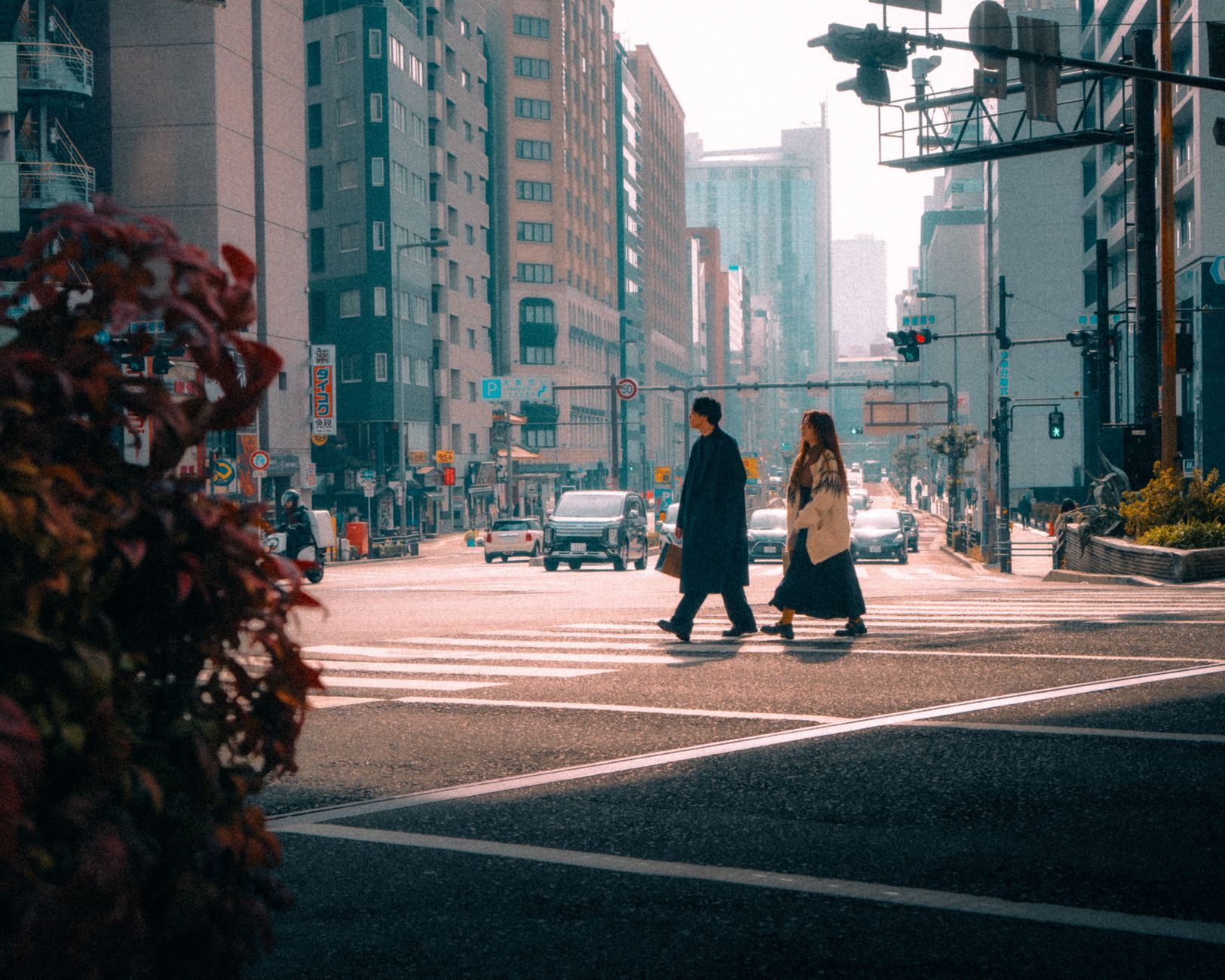Pedestrians waiting patiently at a red traffic light on an empty Tokyo street intersection during daytime.