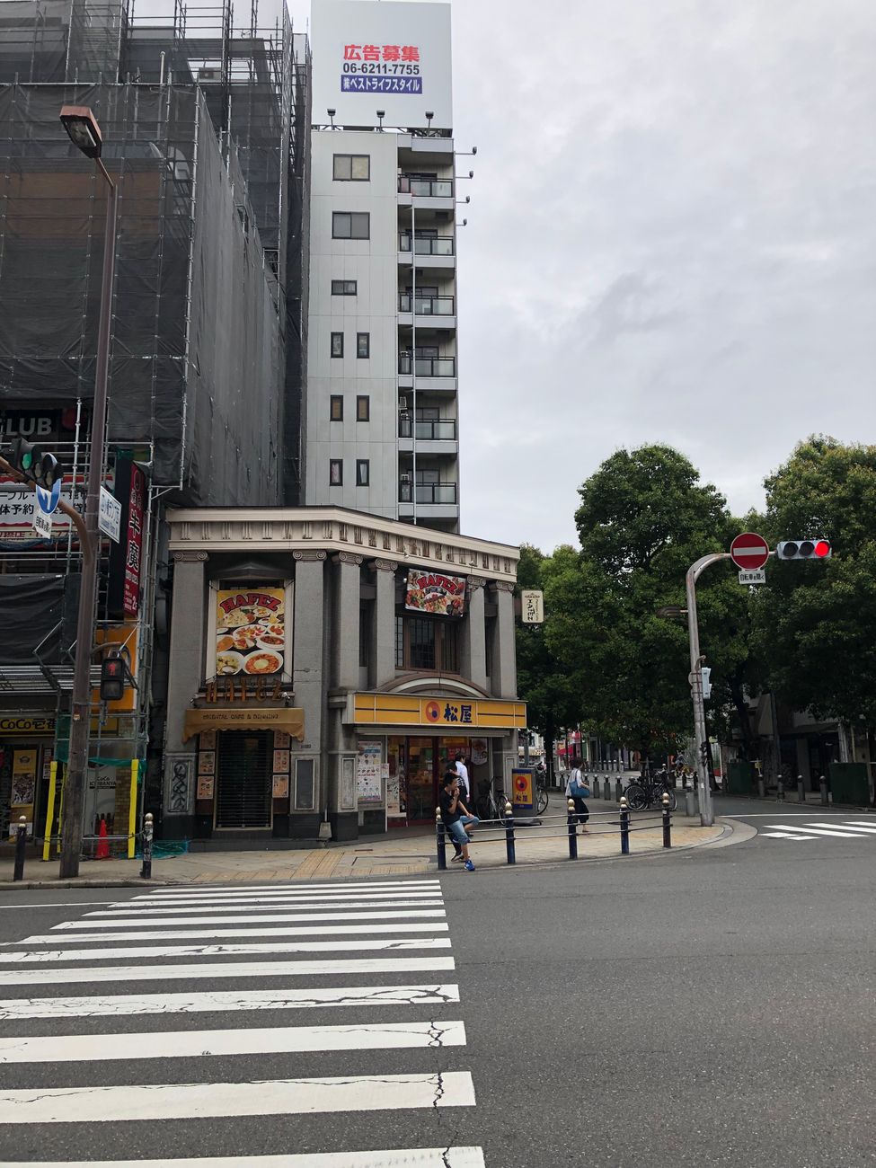 Pedestrians waiting patiently at a red traffic light on an empty Tokyo street intersection during daytime.