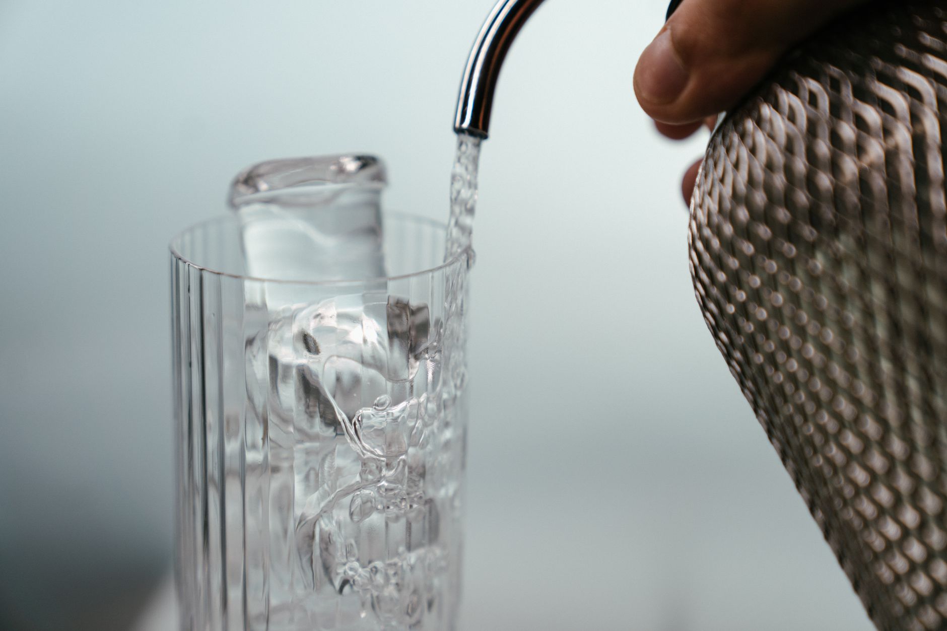 Person pouring clear tap water from a modern faucet into a transparent glass in a Japanese kitchen