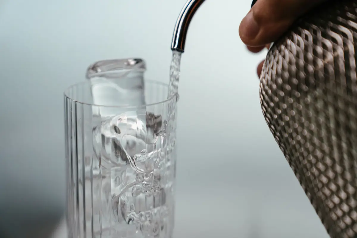 Person pouring clear tap water from a modern faucet into a transparent glass in a Japanese kitchen
