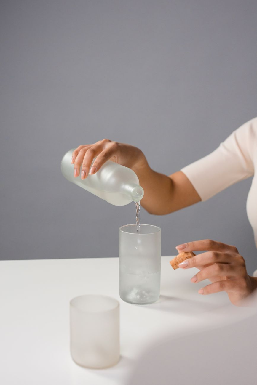 Person pouring clear tap water from a modern faucet into a transparent glass in a Japanese kitchen