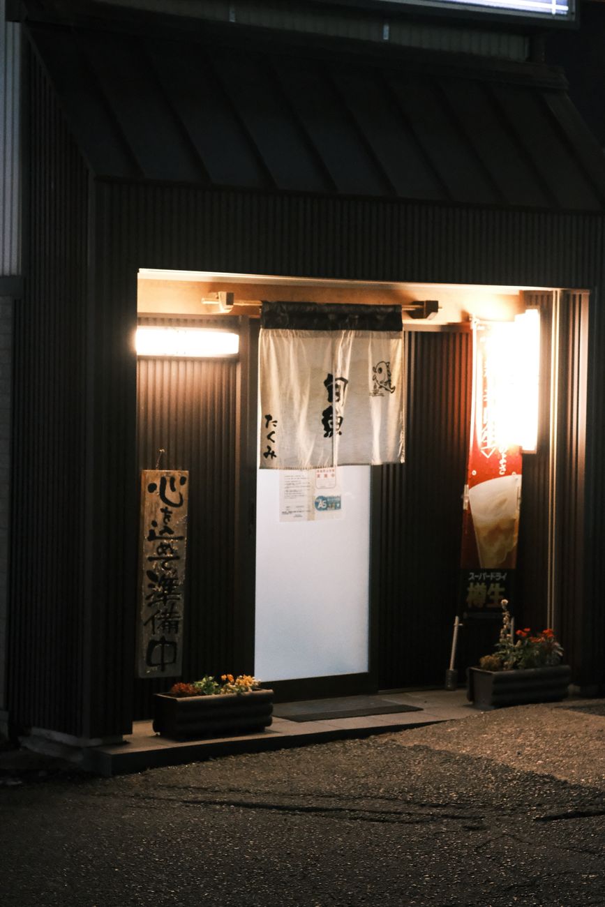 Traditional Japanese onsen entrance with wooden signage displaying bathing rules and tattoo prohibition symbol in natural hot spring setting.