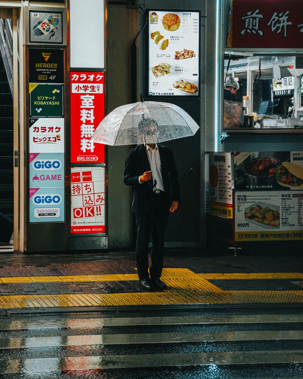 Wet umbrella being inserted into a tall plastic sleeve dispenser at the entrance of a Japanese department store.