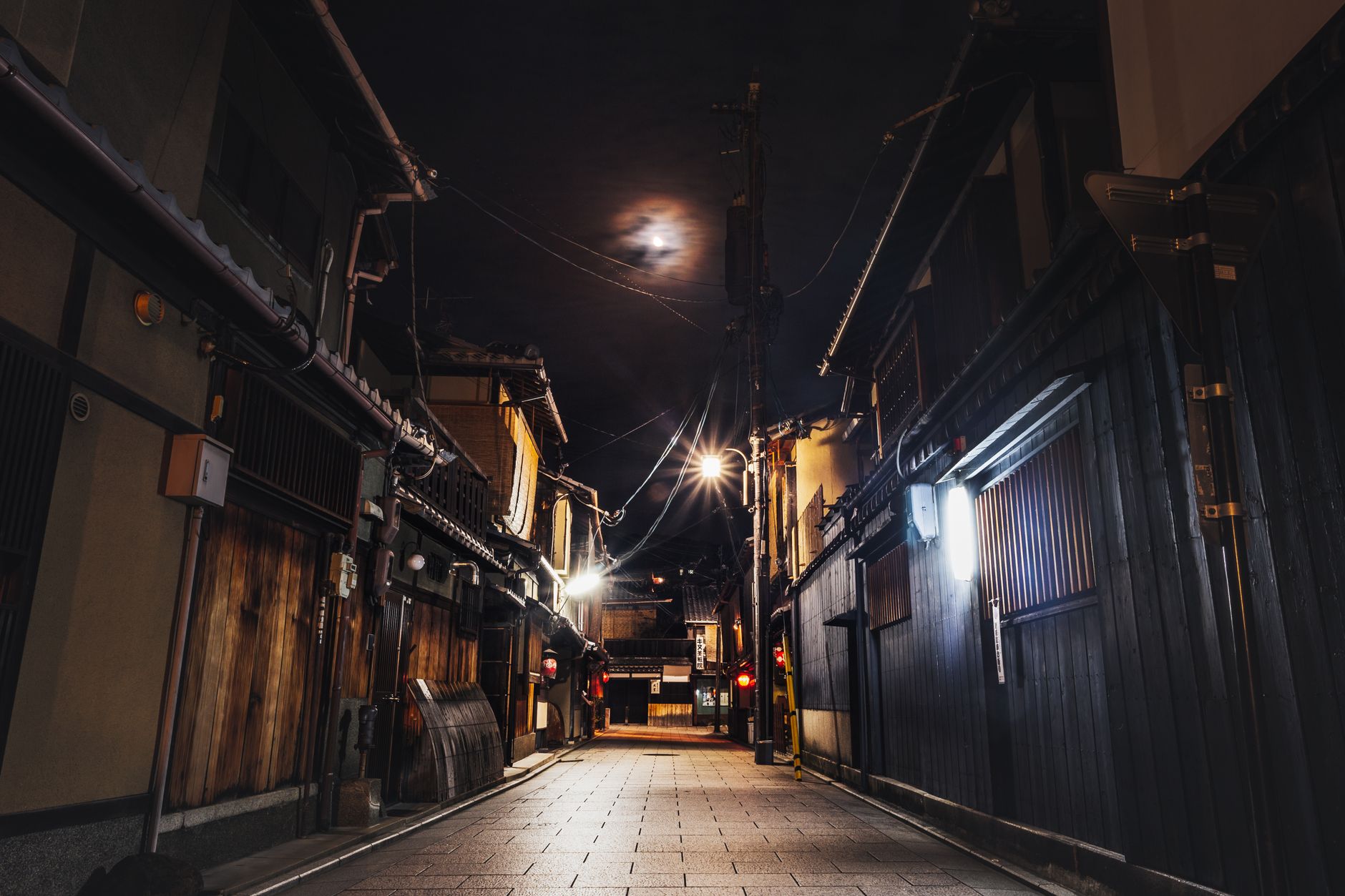 Traditional wooden machiya townhouses line a narrow stone-paved street in Kyoto's historic Higashiyama district at dusk.