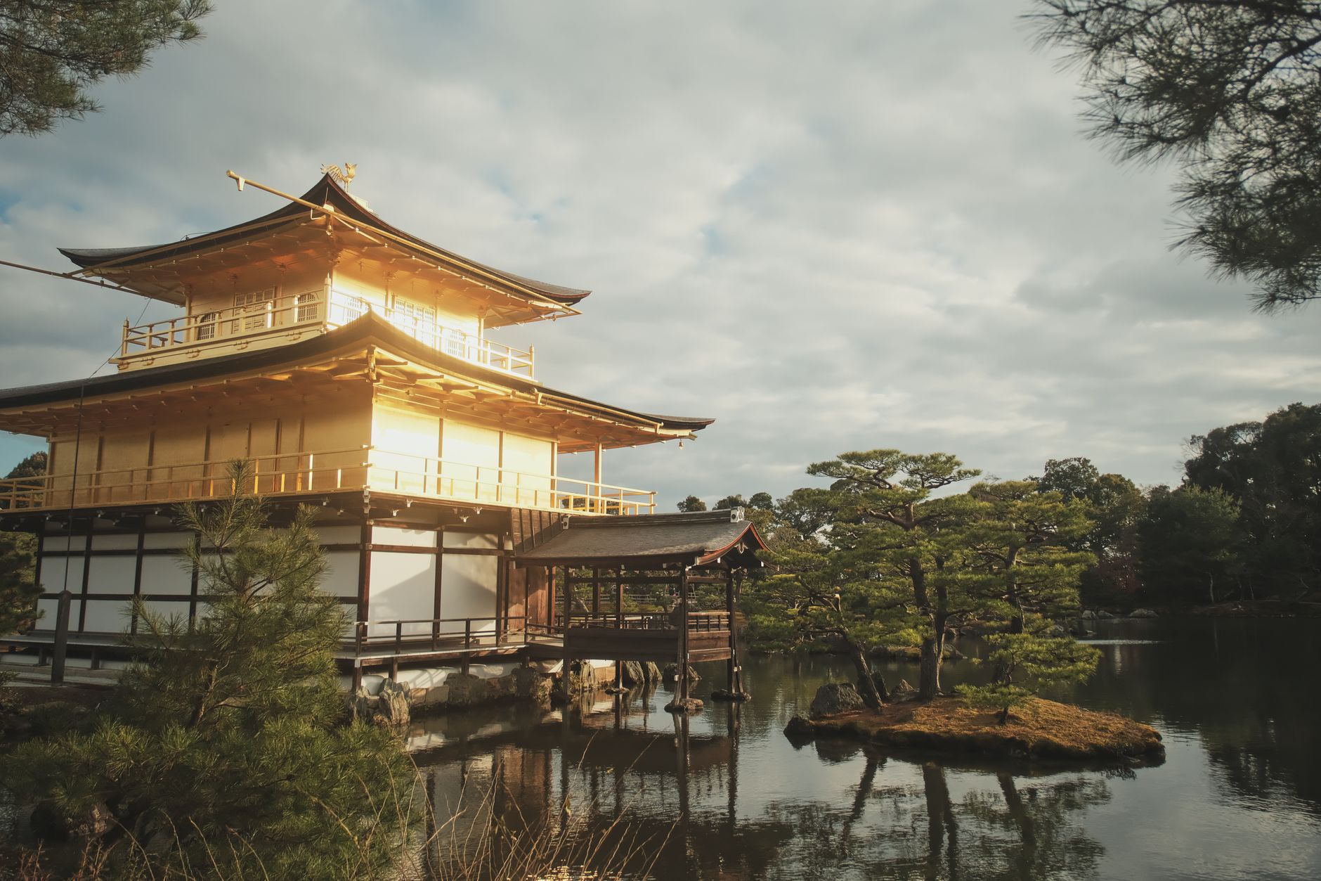 Traditional wooden pagoda rising above stone pathway lined with red torii gates in historic Kyoto temple district at sunset.