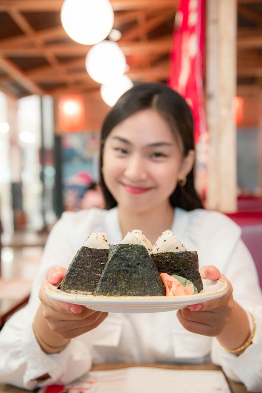 Person holding a traditional Japanese rice bowl in both hands while eating with chopsticks at a dining table.