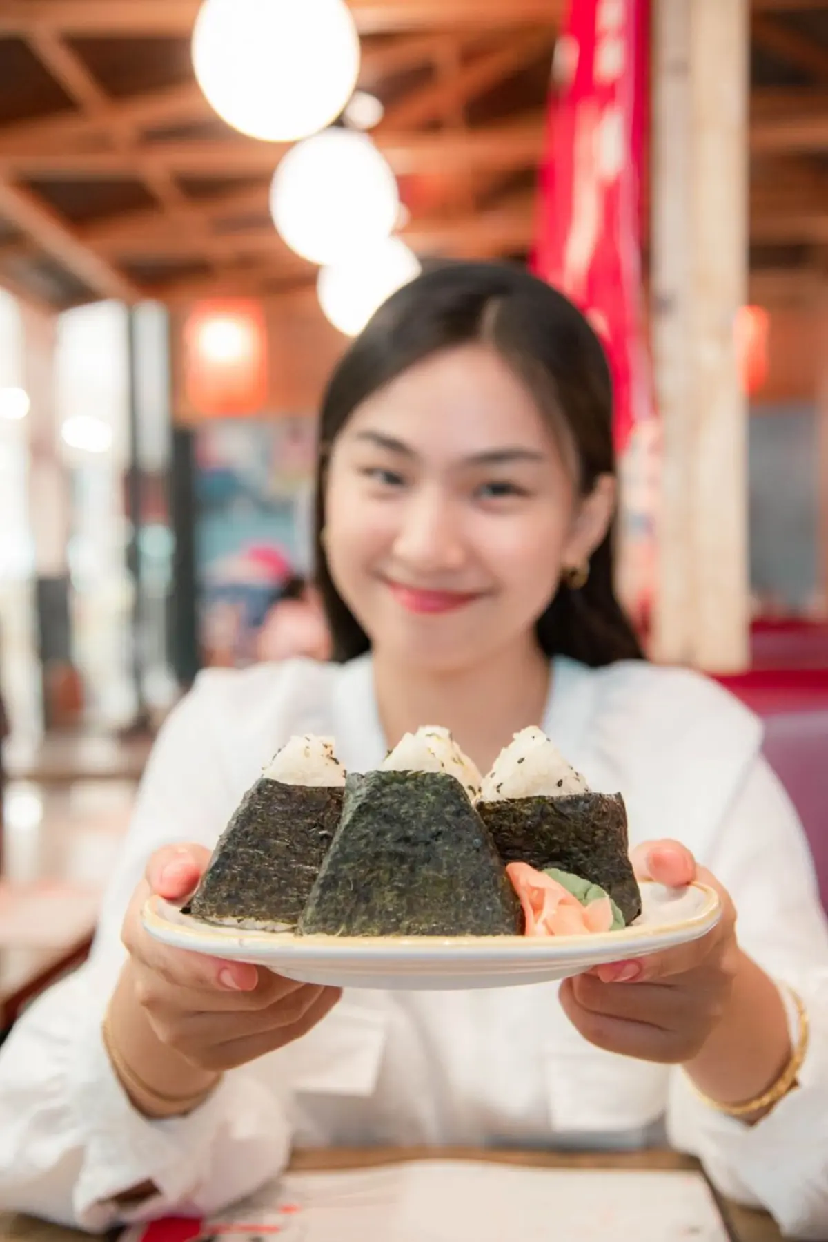 Person holding a traditional Japanese rice bowl in both hands while eating with chopsticks at a dining table.