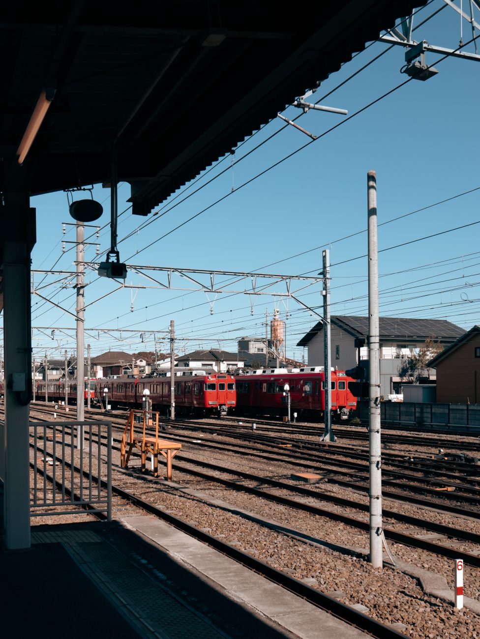 Japanese train conductor in uniform performing pointing and calling gesture toward departure board on railway platform.