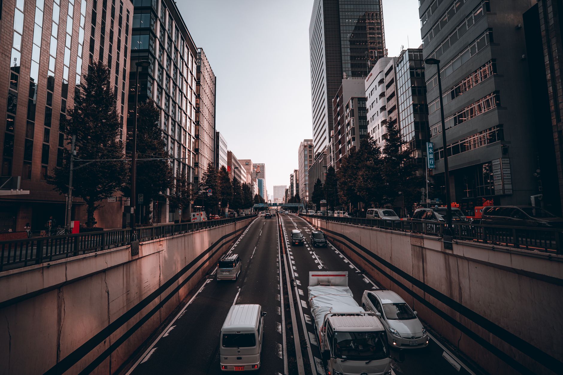 Busy Tokyo intersection with cars driving on the left side of the road beneath towering buildings and pedestrian crossings.