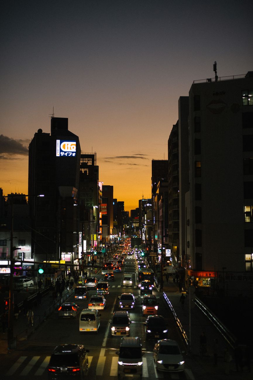 Busy Tokyo intersection with cars driving on the left side of the road beneath towering buildings and pedestrian crossings.