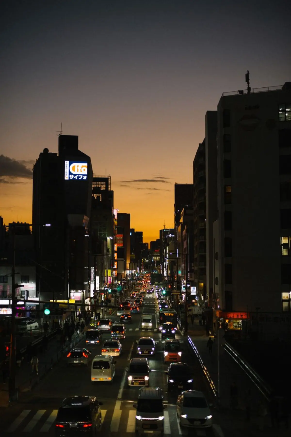 Busy Tokyo intersection with cars driving on the left side of the road beneath towering buildings and pedestrian crossings.