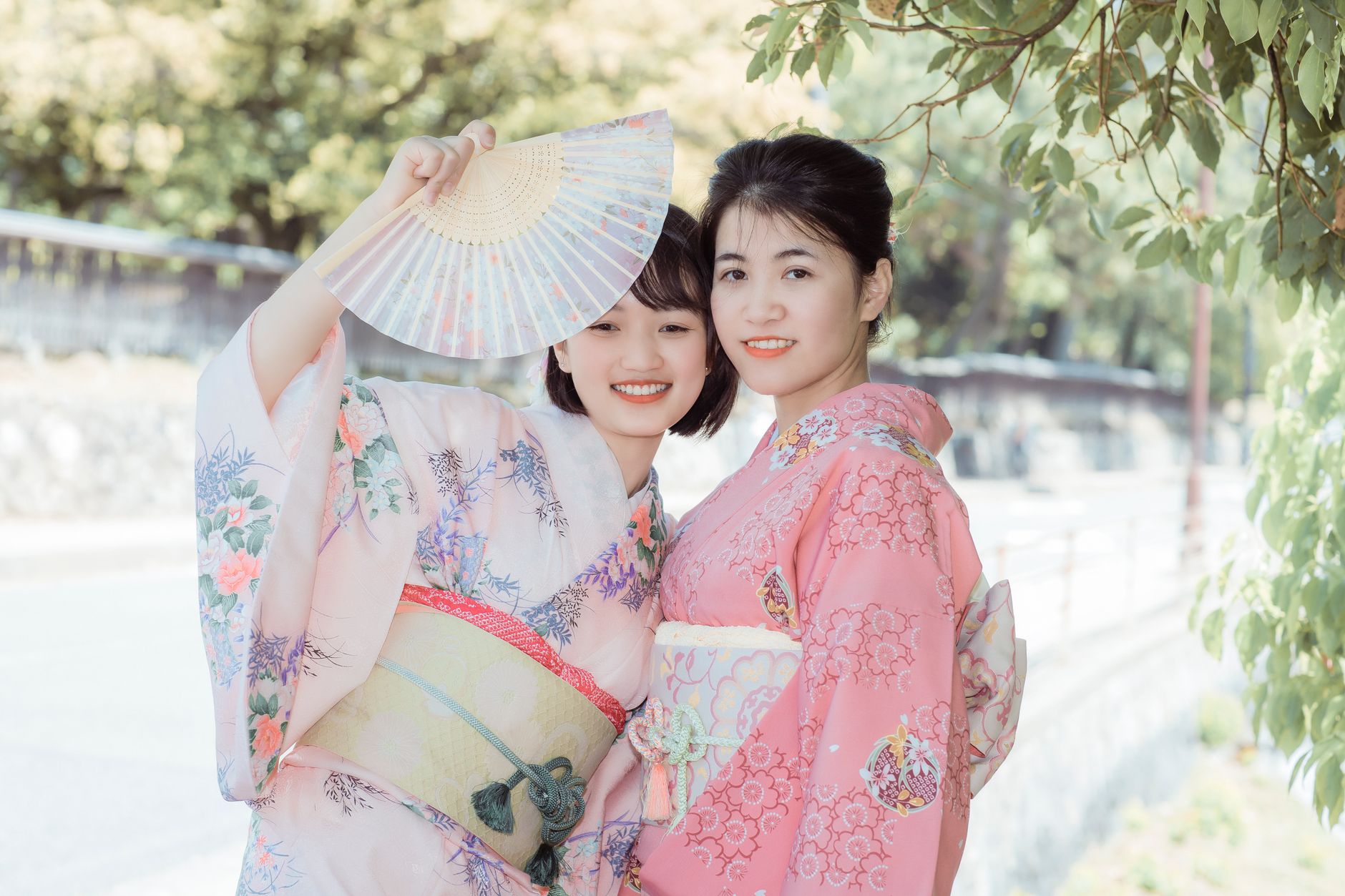 Young Japanese women wearing colorful patterned yukata with obi sashes walk together through a lantern-lit summer festival at dusk.