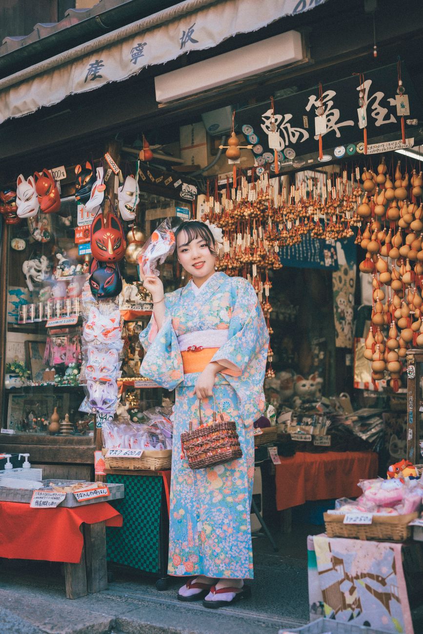 Young Japanese women wearing colorful patterned yukata with obi sashes walk together through a lantern-lit summer festival at dusk.