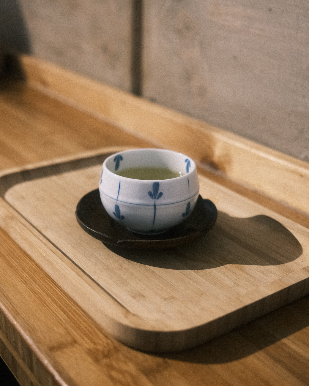Ceramic tea cup filled with green tea on wooden tray beside water glass in traditional Japanese restaurant setting.