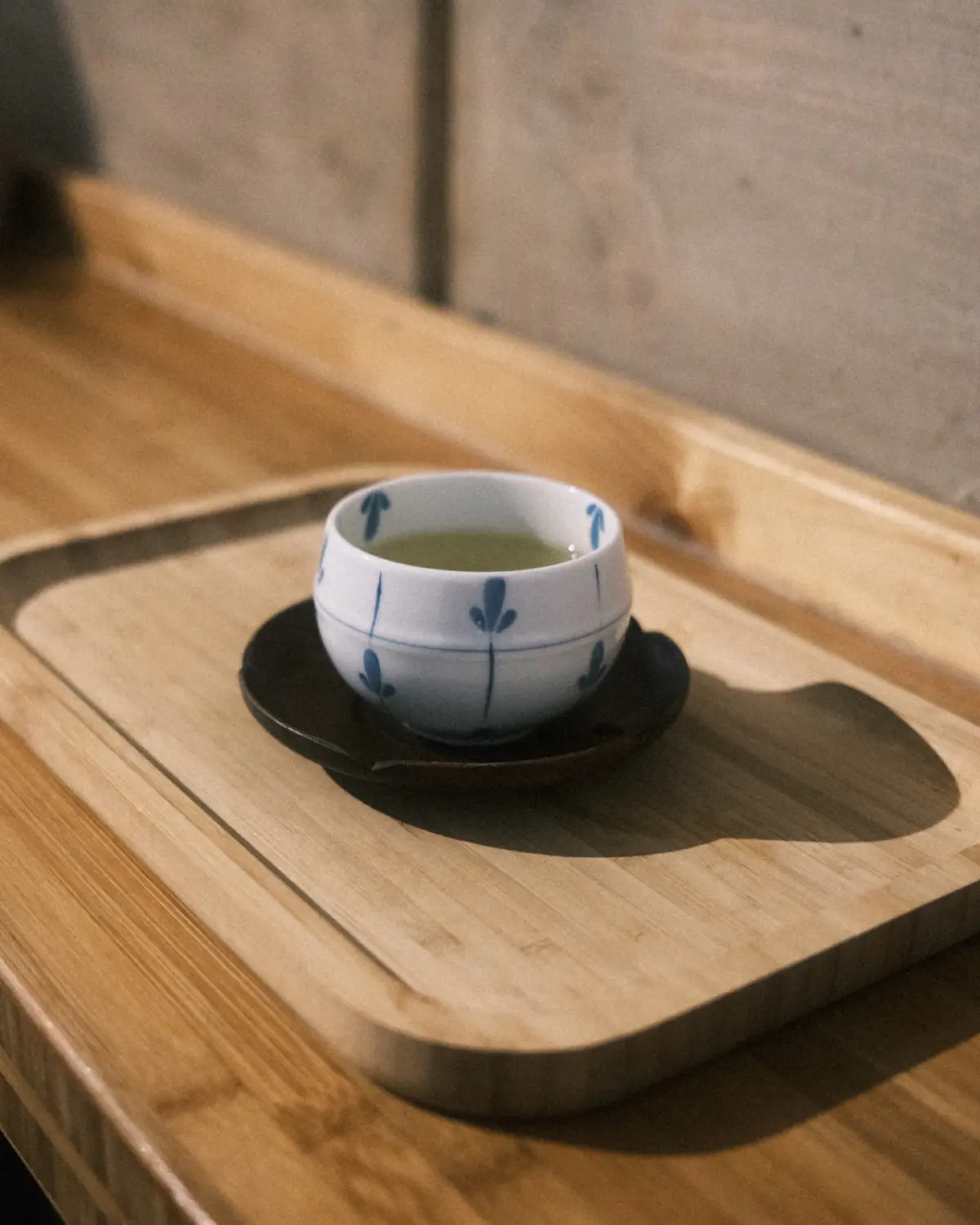 Ceramic tea cup filled with green tea on wooden tray beside water glass in traditional Japanese restaurant setting.