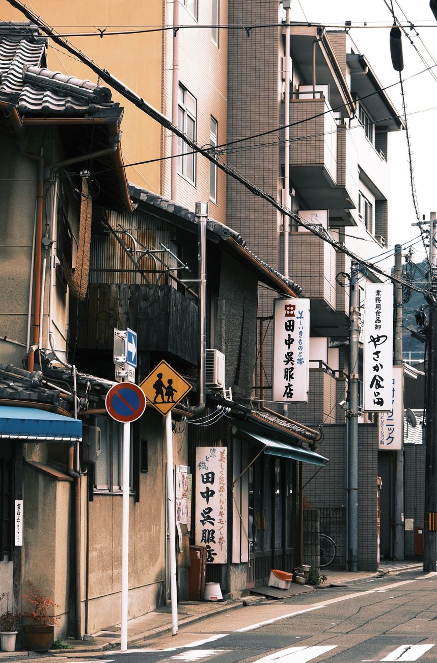 Narrow residential street in Tokyo with utility poles, vending machines, and small address number plates on building walls.