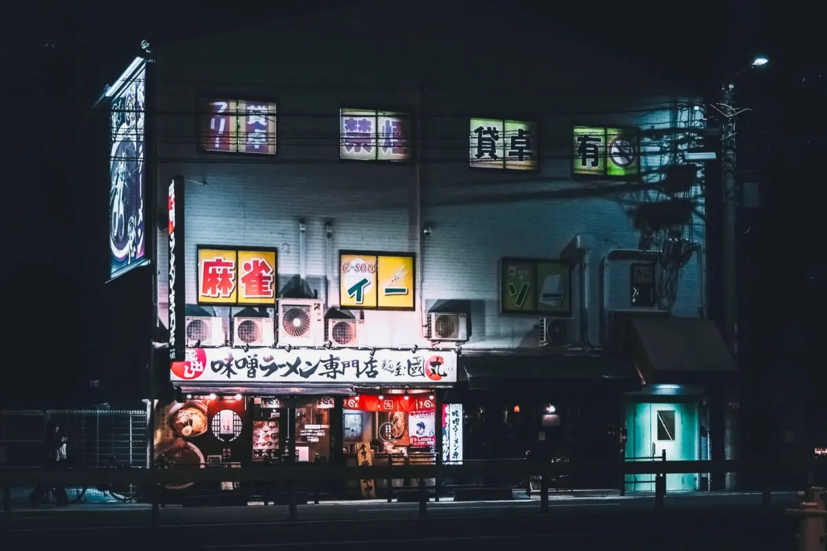 Customer inserting coins into a traditional Japanese ticket vending machine at the entrance of a small ramen restaurant.