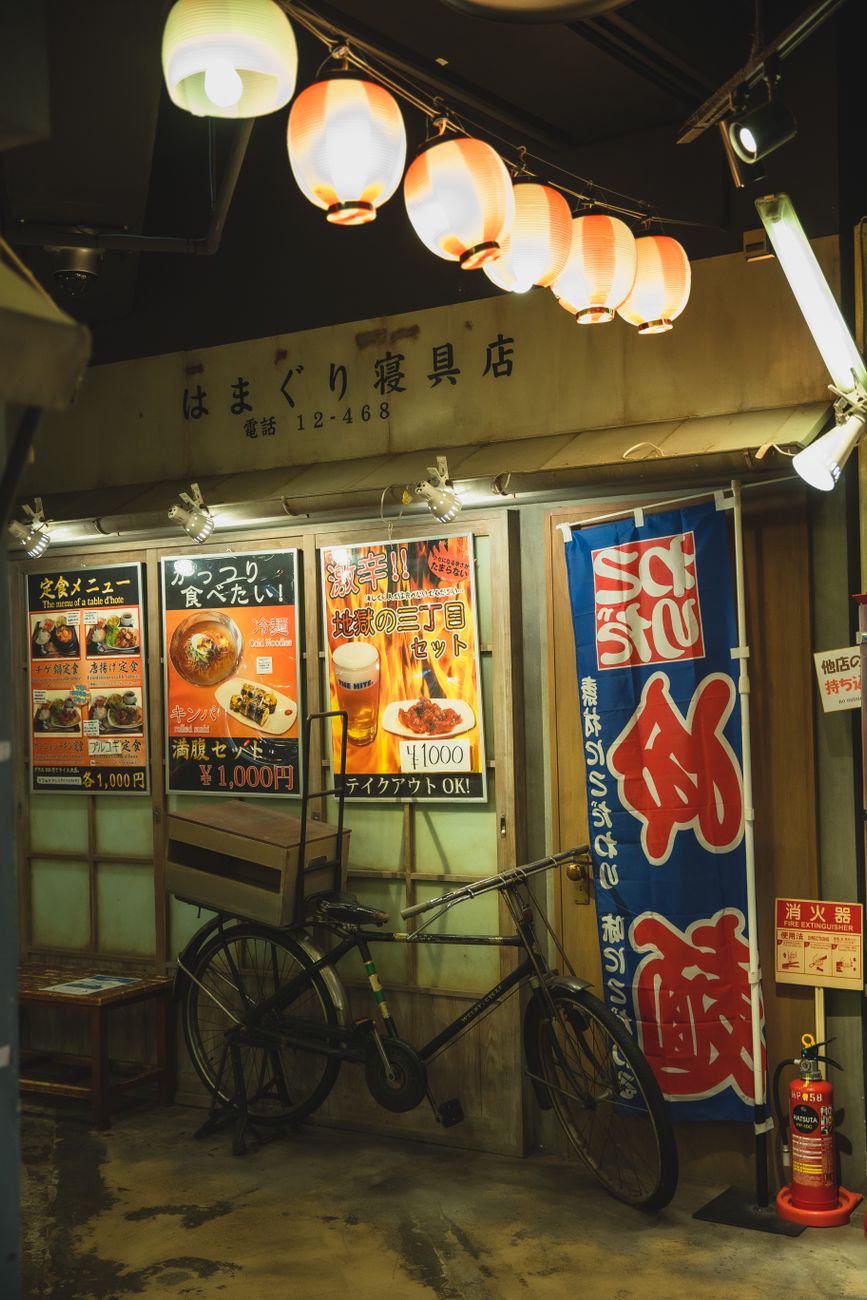 Customer inserting coins into a traditional Japanese ticket vending machine at the entrance of a small ramen restaurant.