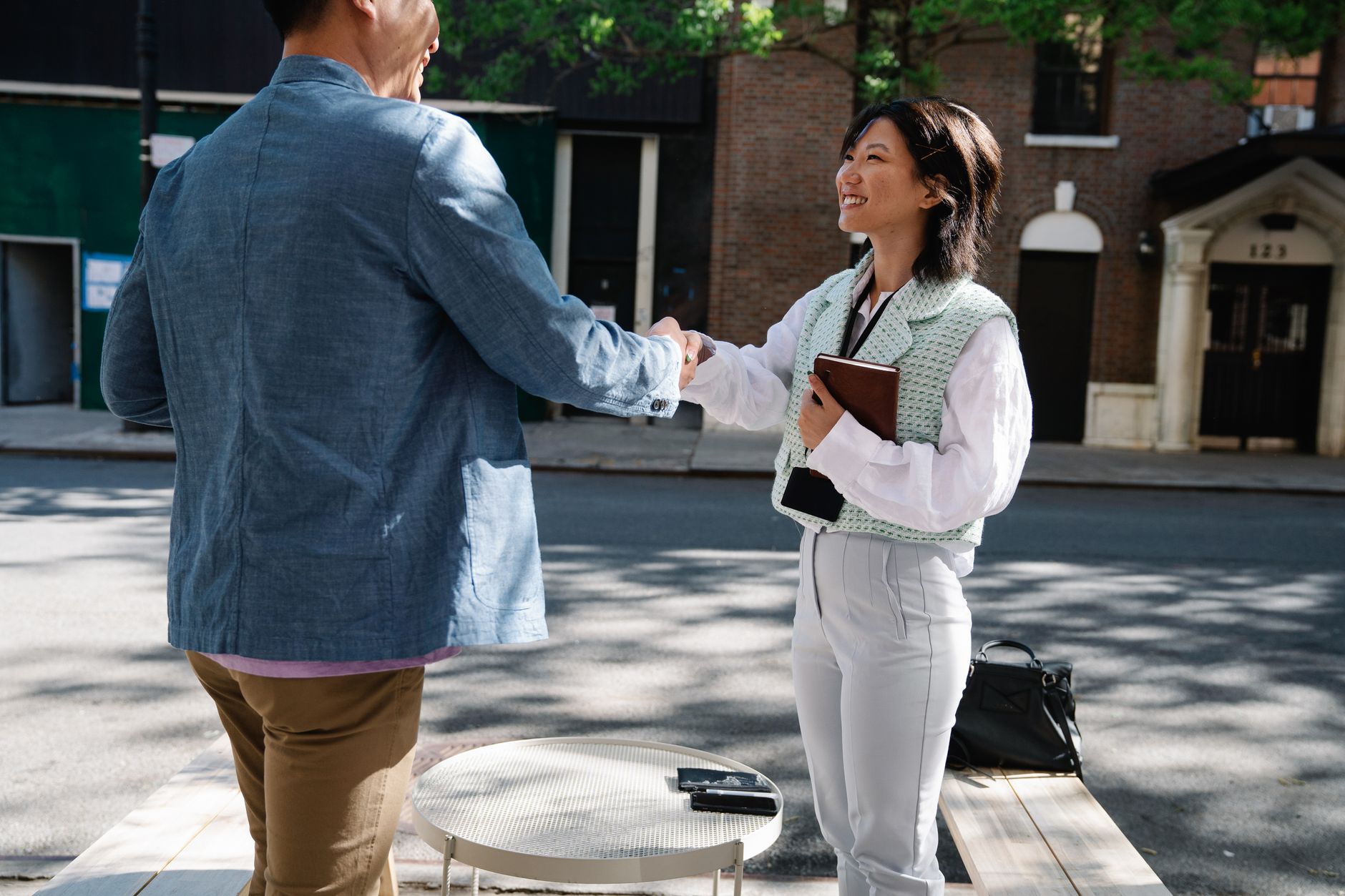 Two Japanese businesspeople in suits exchange business cards with both hands while bowing slightly in a modern office setting.