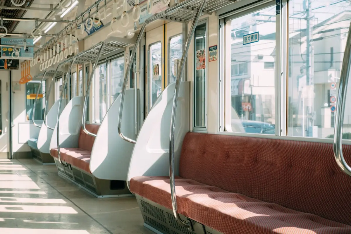 Elderly passenger seated in designated priority seat area marked with pink upholstery near Japanese train door.